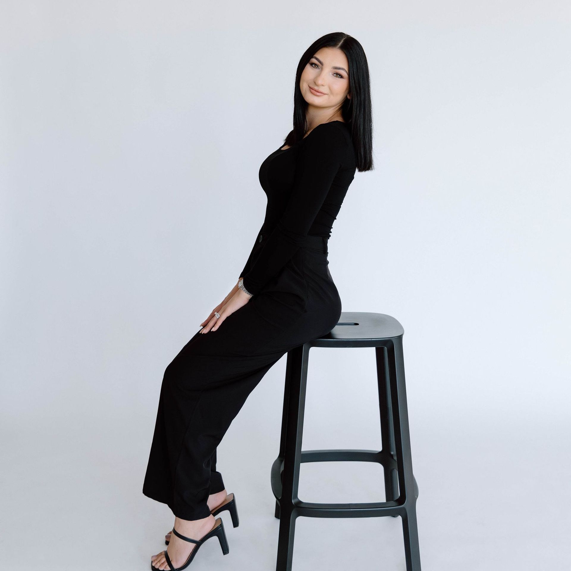 A woman in a black dress is sitting on a stool.