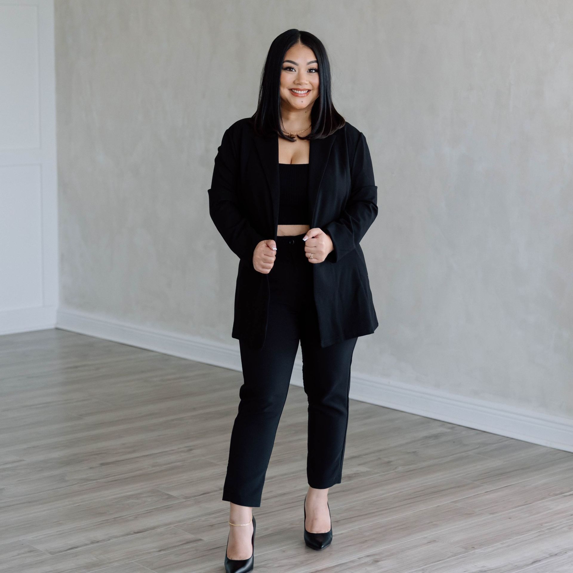 A woman is standing in a room wearing a black suit and heels.