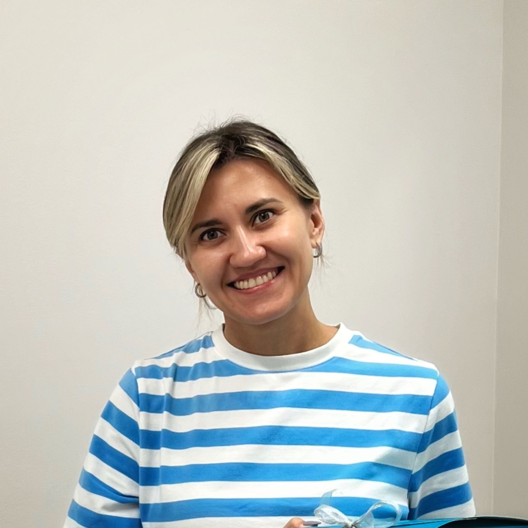 A woman is wearing a blue and white striped shirt and smiling.