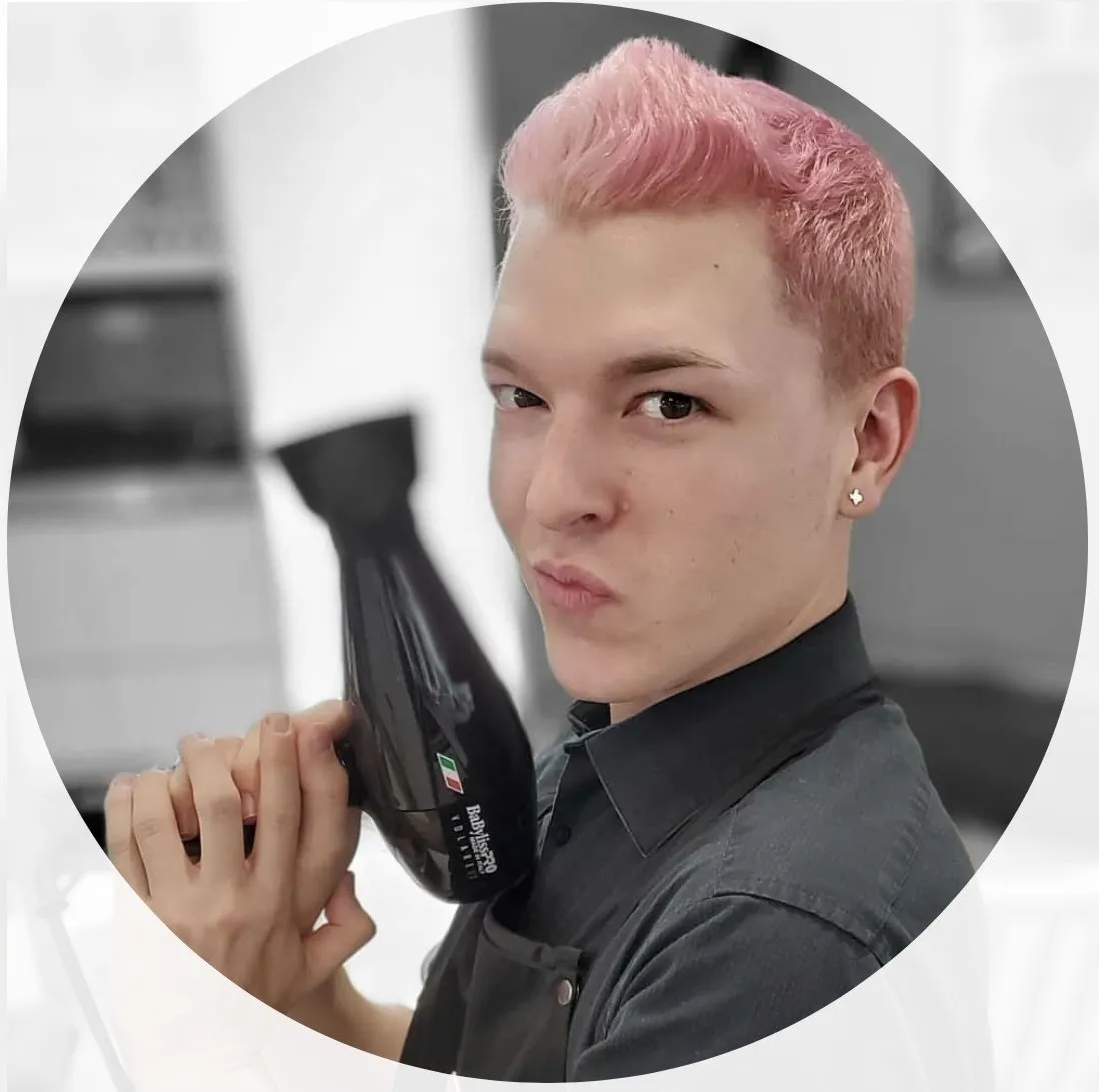 A man with pink hair is holding a hair dryer in his hand.