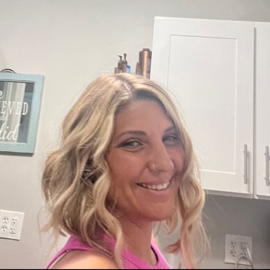 A woman in a pink tank top is smiling in a kitchen.