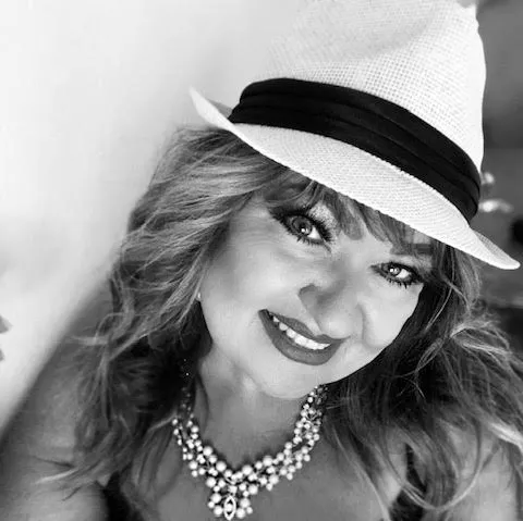 A woman wearing a hat and a necklace is smiling in a black and white photo.