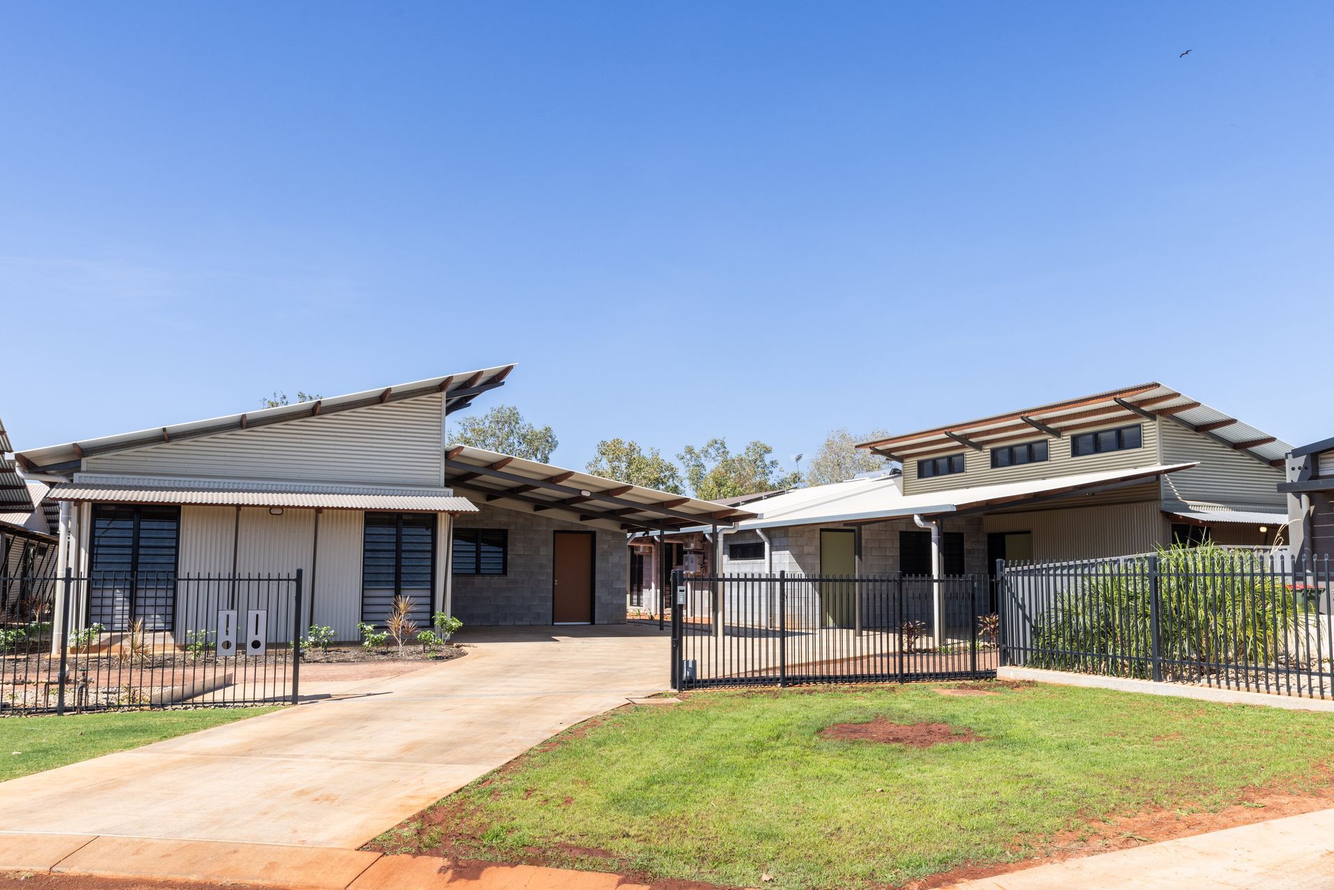 Houses with unusual angled roofs and corrugated metal, driveway, and a green lawn.