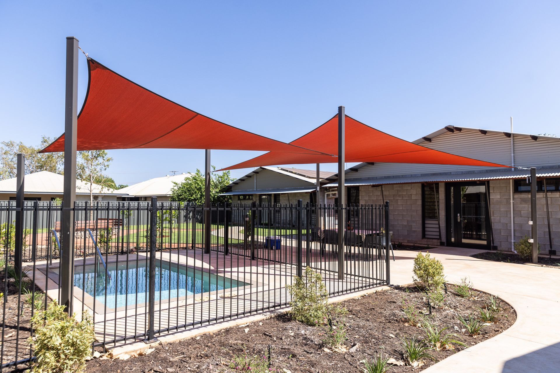 Two red shade sails over a small pool, surrounded by a black fence.