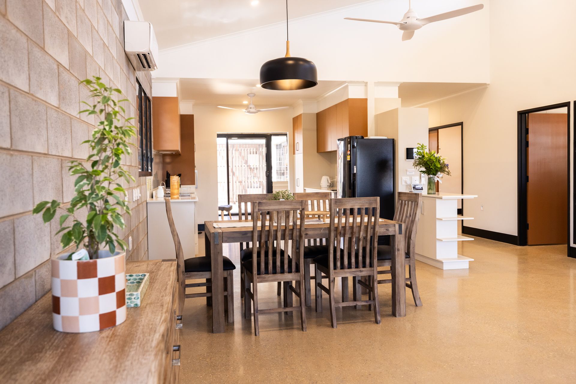 Dining room with a wooden table, chairs, and an open kitchen.  A plant sits on a wooden counter.