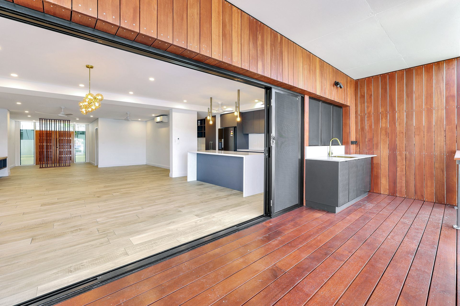 Wooden deck with open sliding doors to modern interior and outdoor kitchen.