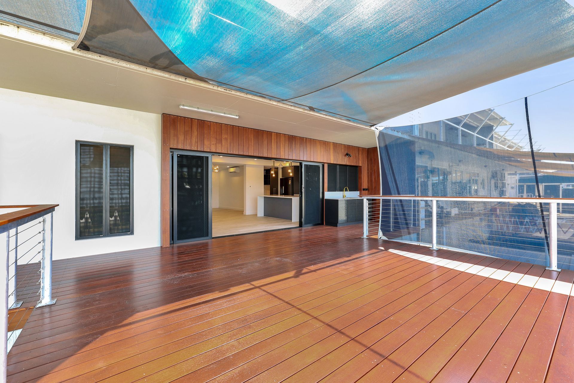 Wooden deck with shade canopy, leading to a bright interior with open doors.