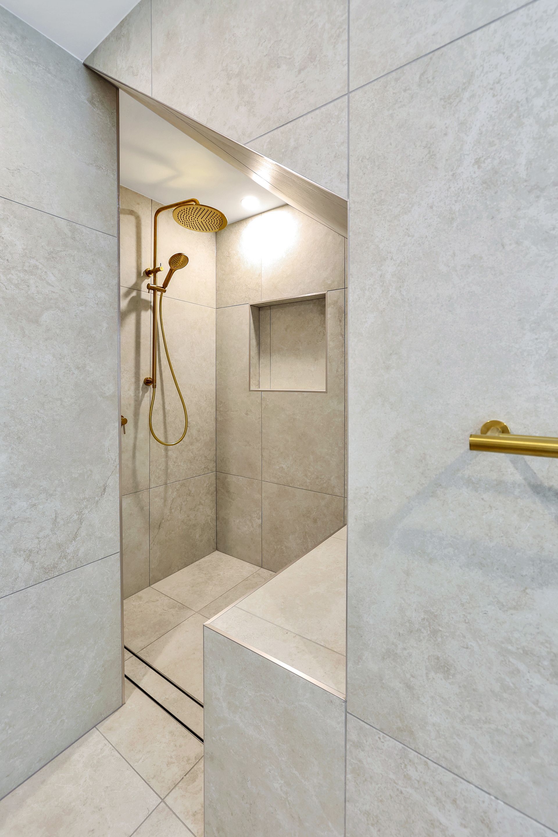 Modern shower with gold fixtures, tiled walls, and a built-in bench.