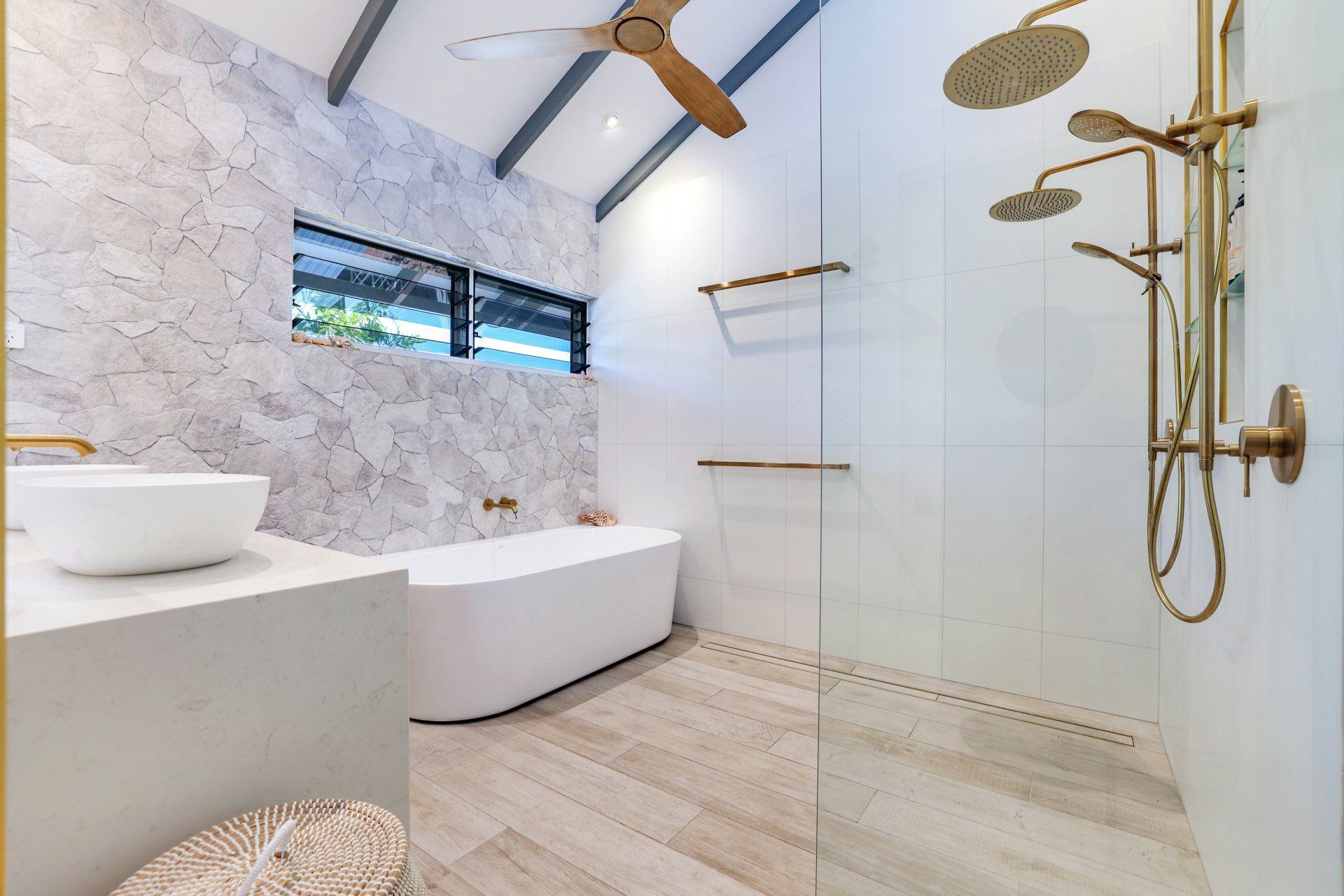 Modern bathroom with marble walls, white bathtub, gold fixtures, and a glass shower.