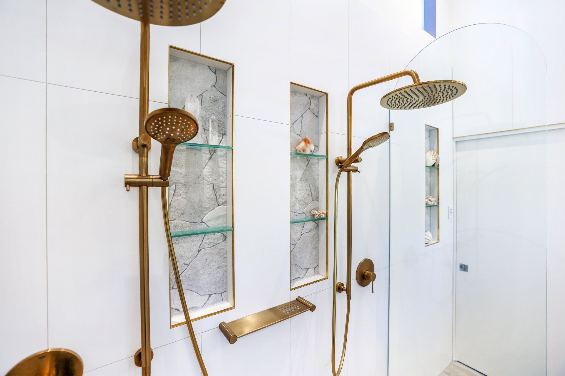 Shower with gold fixtures and recessed shelves against white tiled wall.