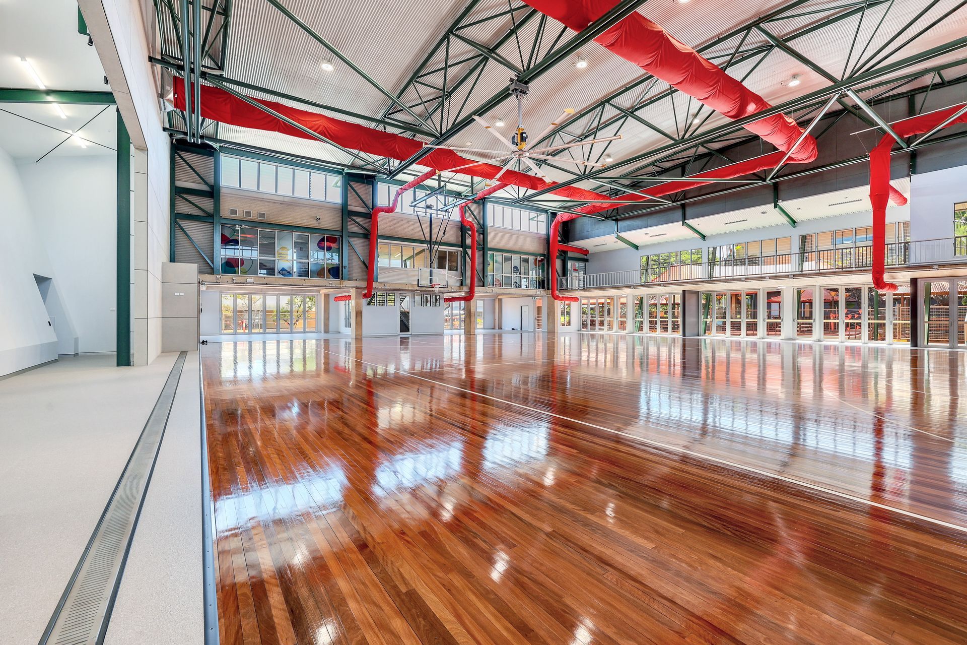 Wooden floored indoor space with large windows, exposed ceiling beams, and red ductwork.