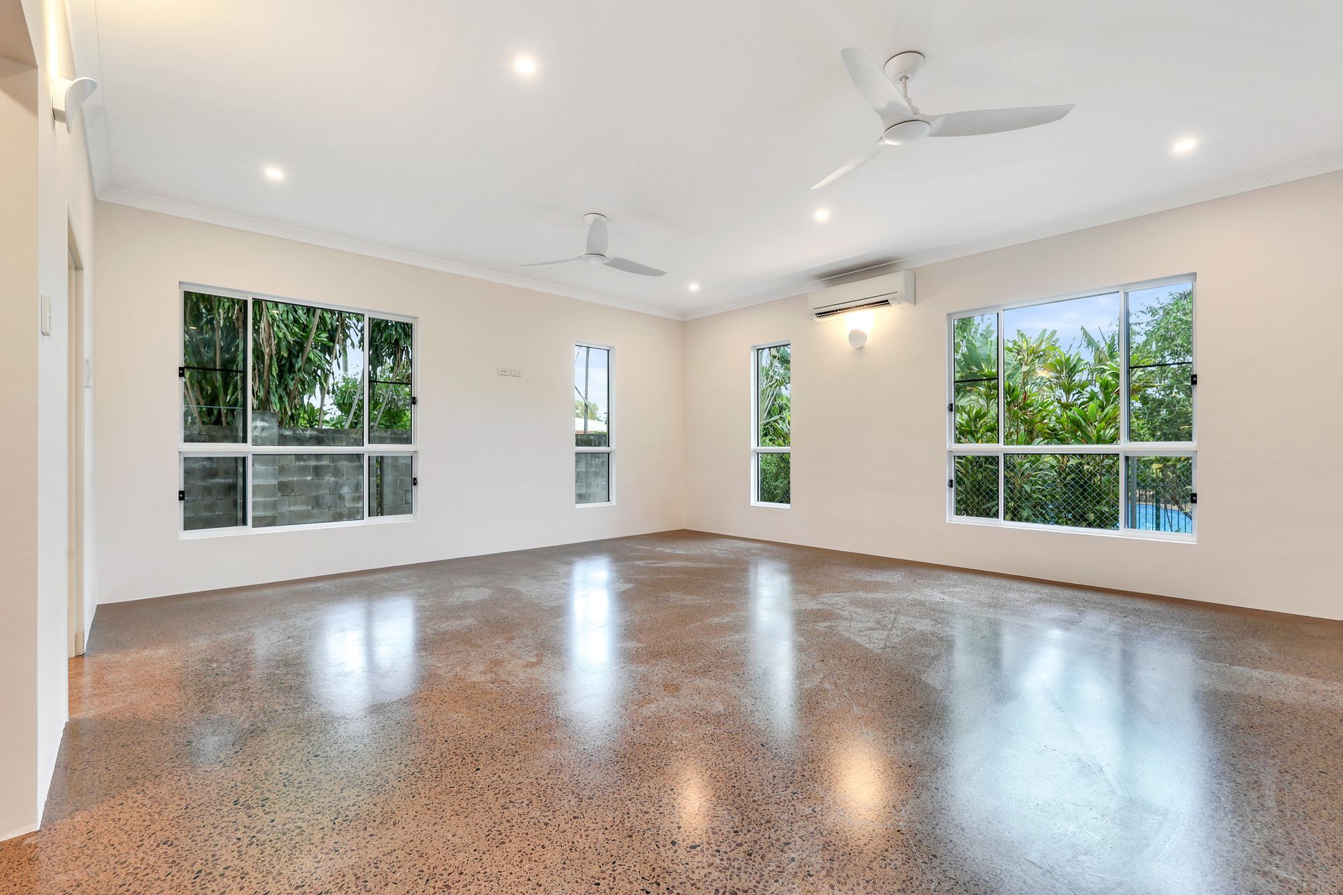 Empty room with polished concrete floor, windows, and ceiling fans.