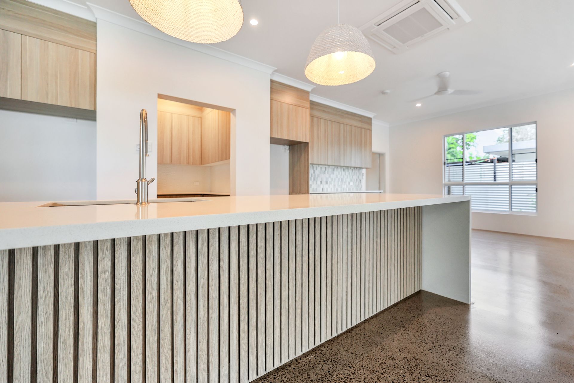 Modern kitchen with light wood cabinets, white countertops, and a textured island.
