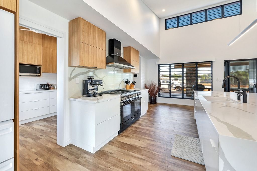 Modern kitchen with light wood cabinets, white counters, black stove, and large windows.