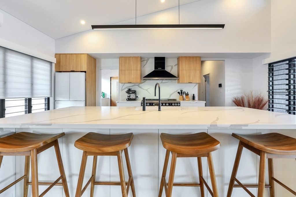 Modern kitchen with wooden stools, light-colored countertop, and cabinetry. Black range hood centered above the stovetop.