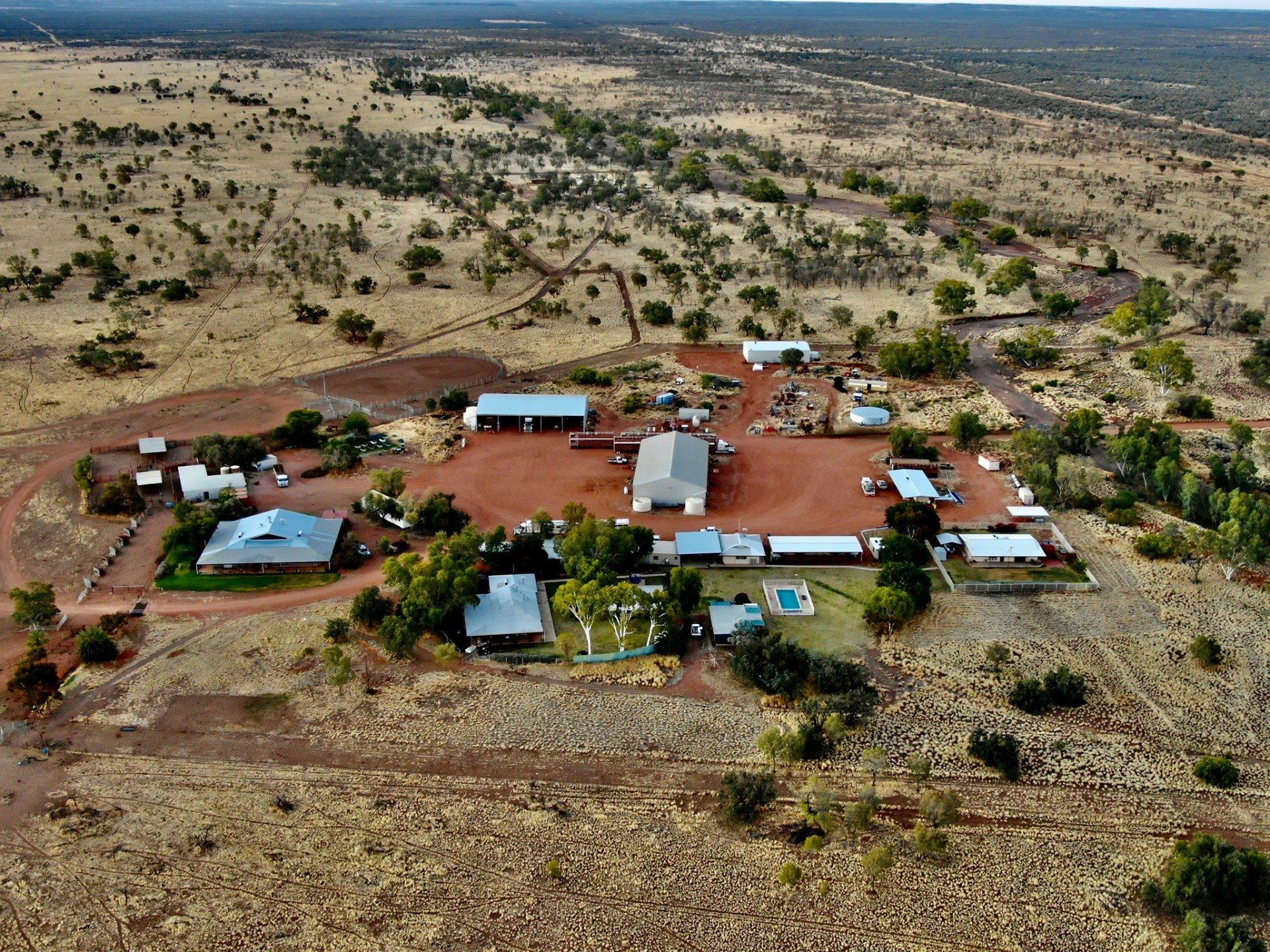 Aerial view of a rural settlement with red soil, buildings, and sparse vegetation.