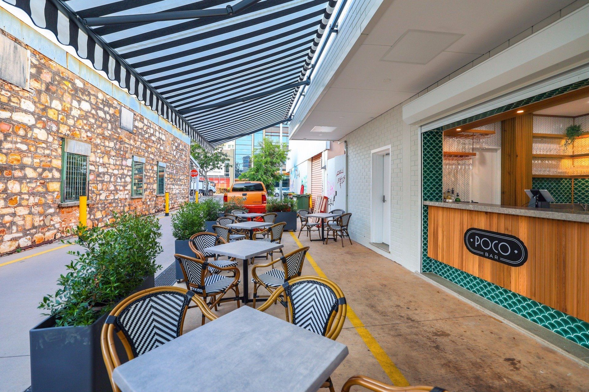 Outdoor cafe with tables, chairs, and a striped awning next to a stone building.