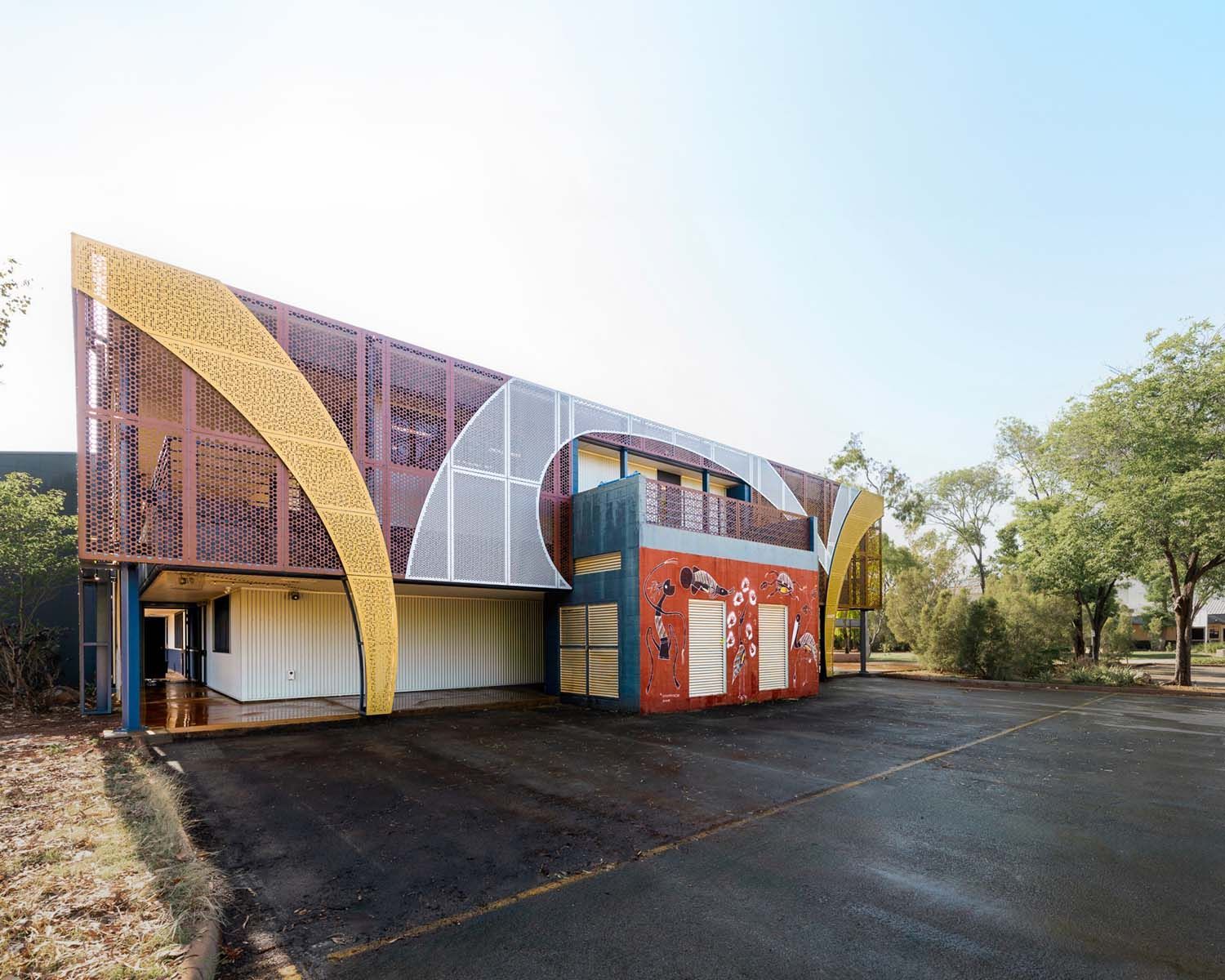 Colourful cladding with abstract shapes on outside of a building with indigenous mural on rest of wall