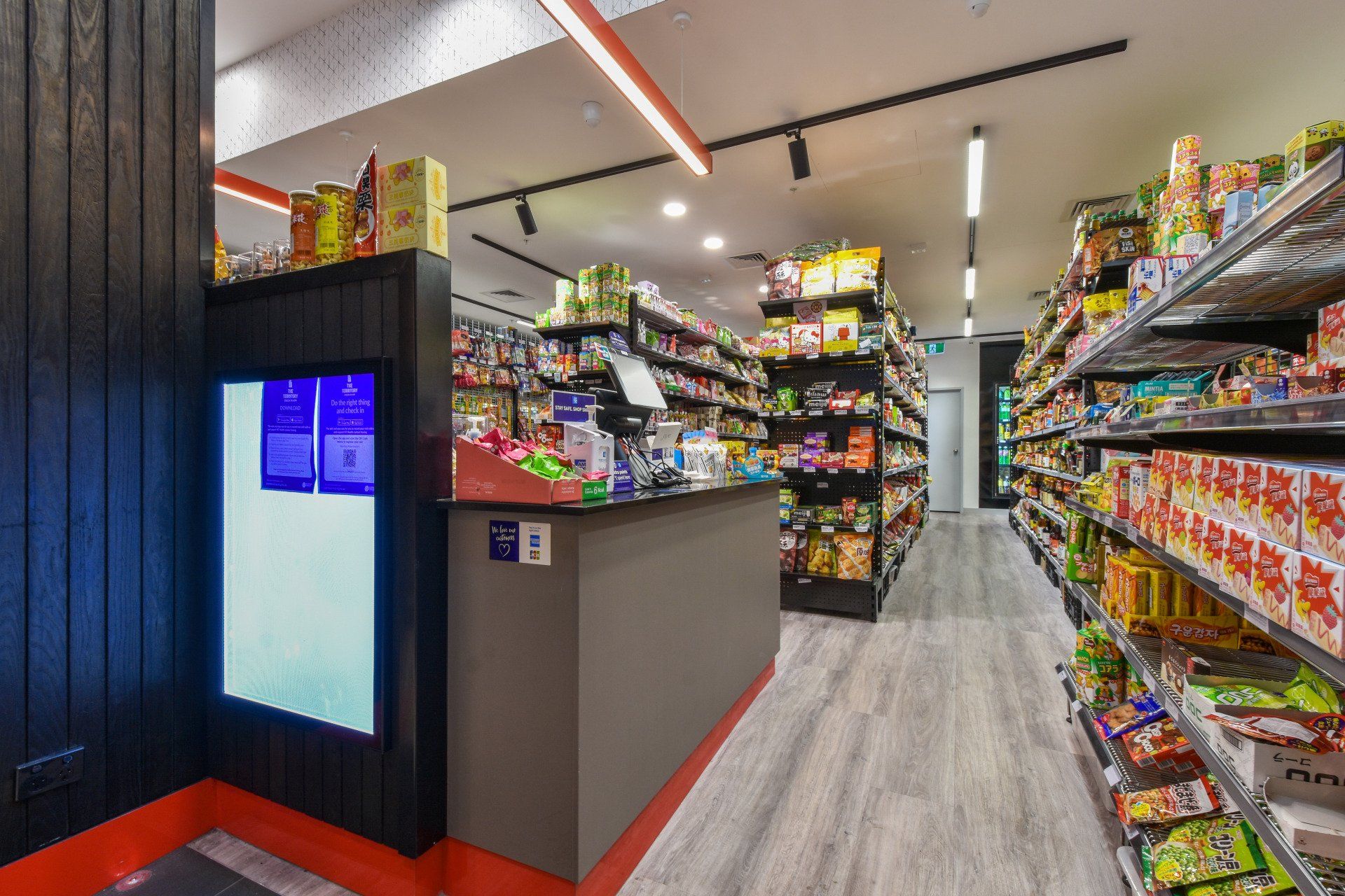 Grocery store interior with products on shelves, a checkout counter, and a digital display.