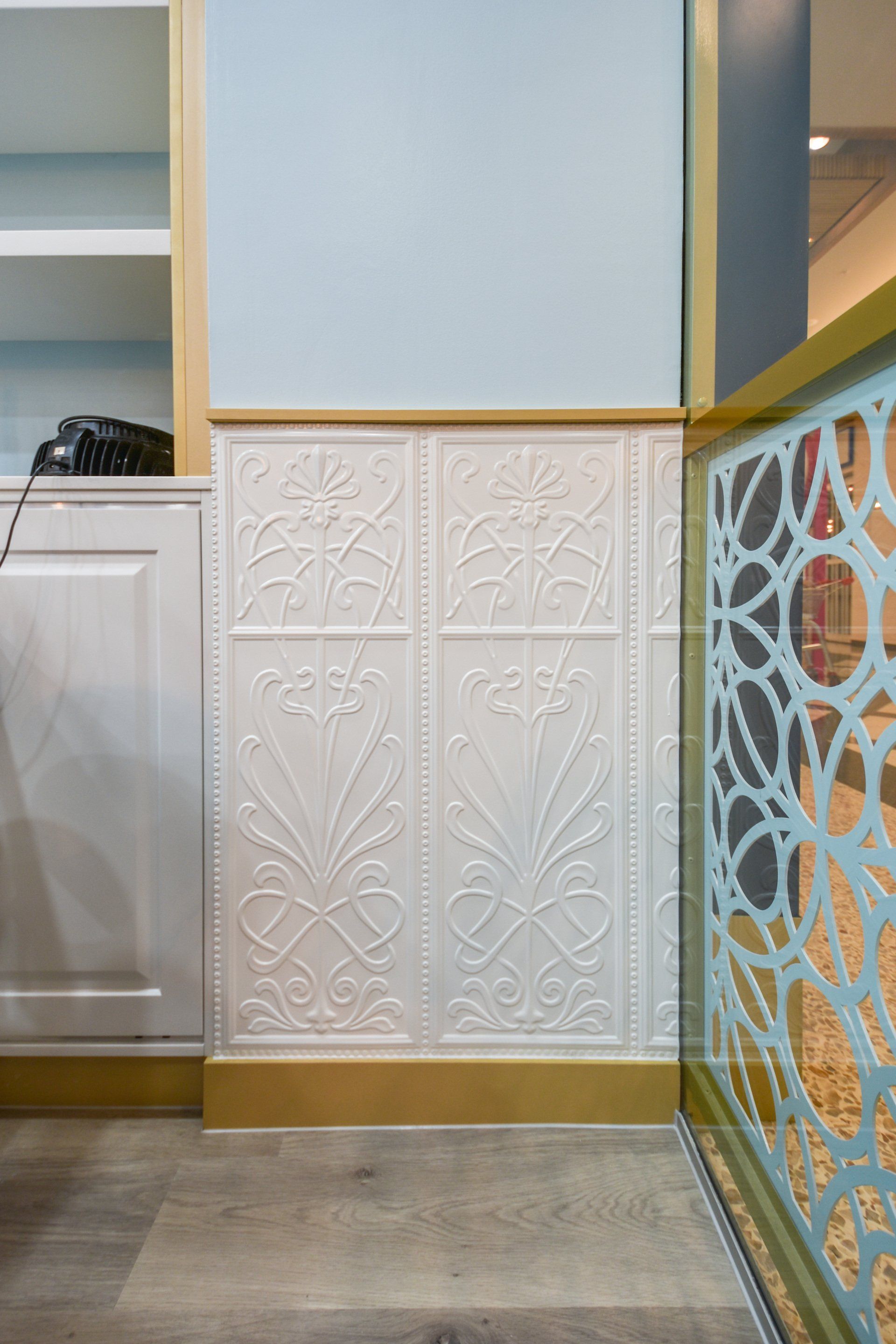 White patterned wall panels with gold trim, adjacent to a decorative light blue railing.