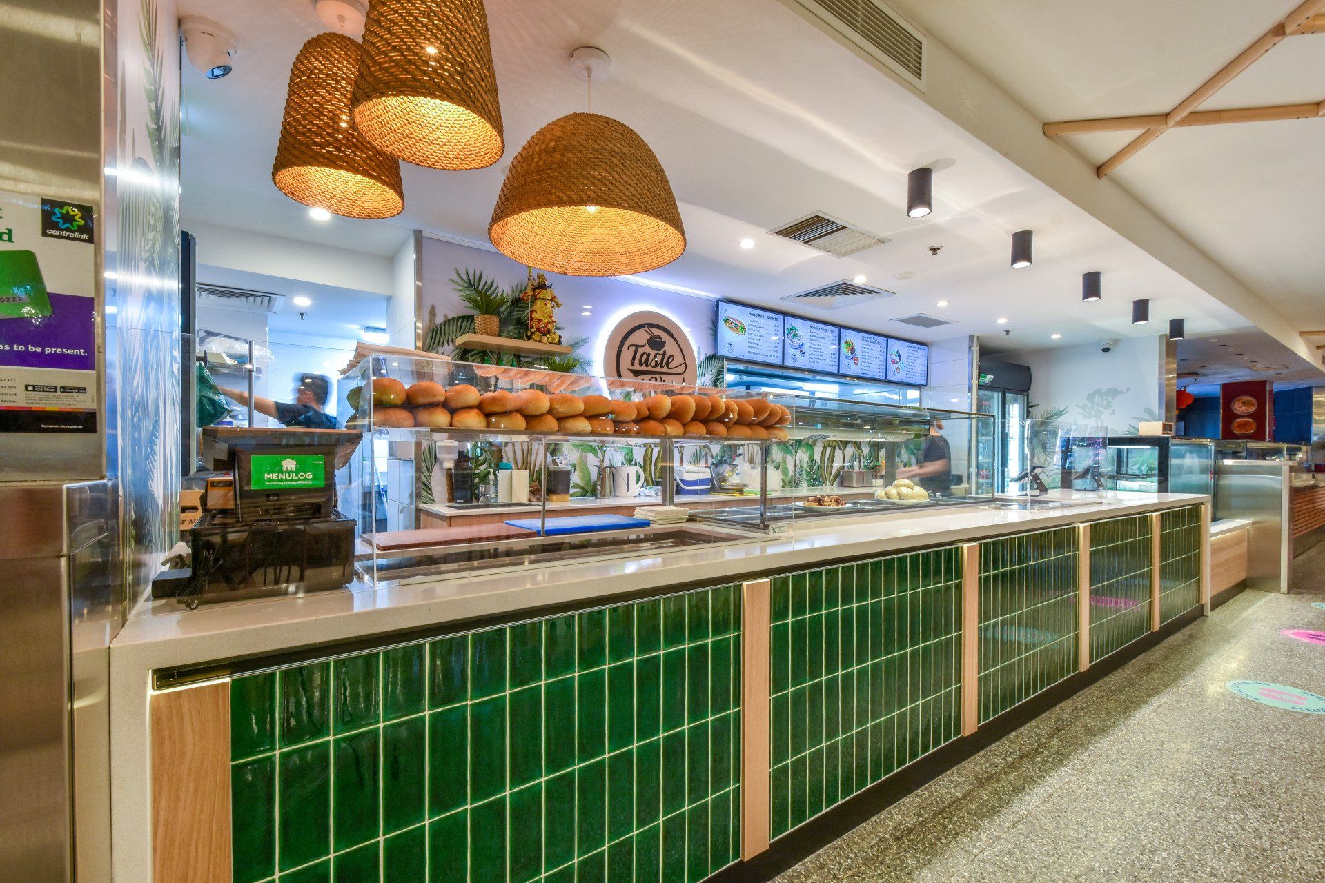 Interior view of a sandwich shop with green tiled counter, warm lighting, and menu displays.