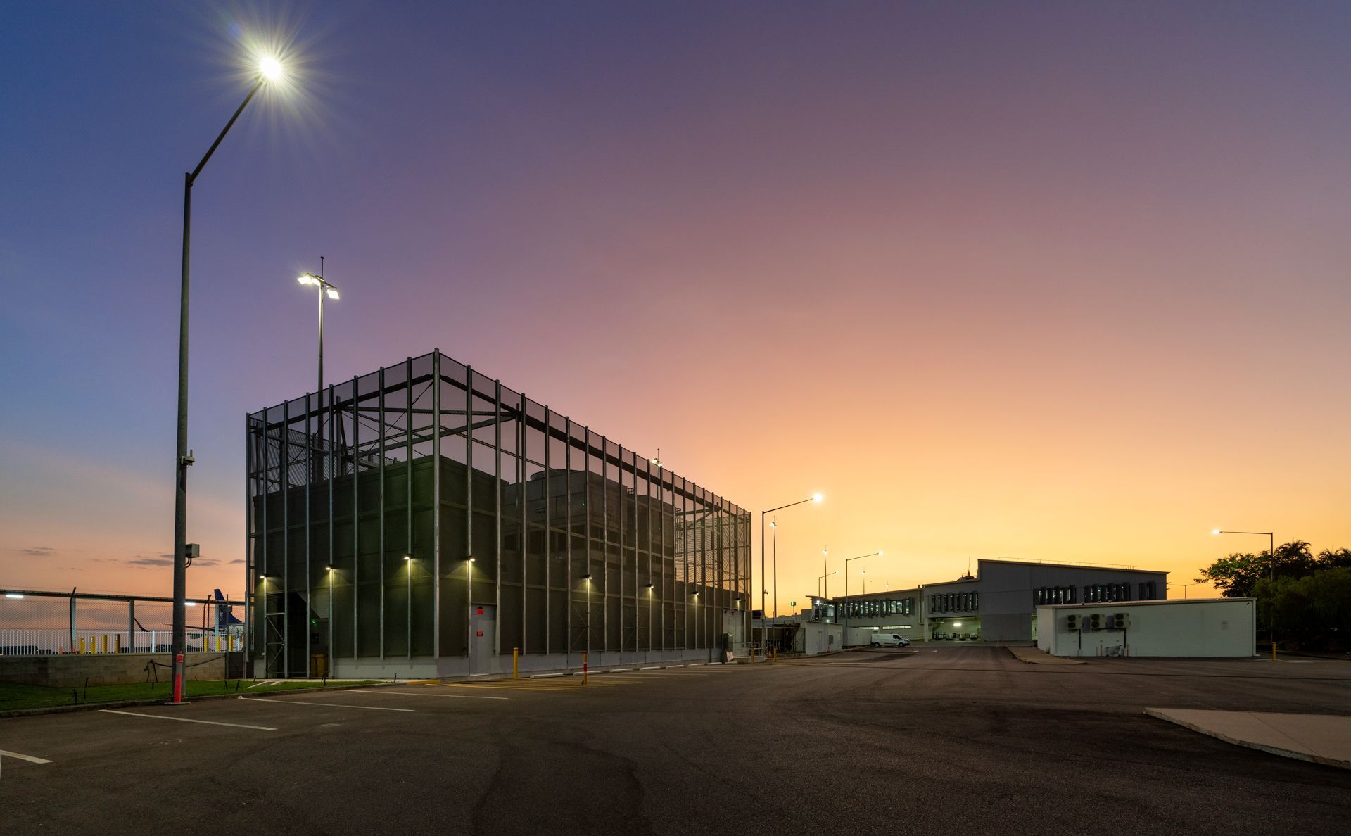 A dusk scene with a secure building and streetlights under a vibrant orange and purple sky.