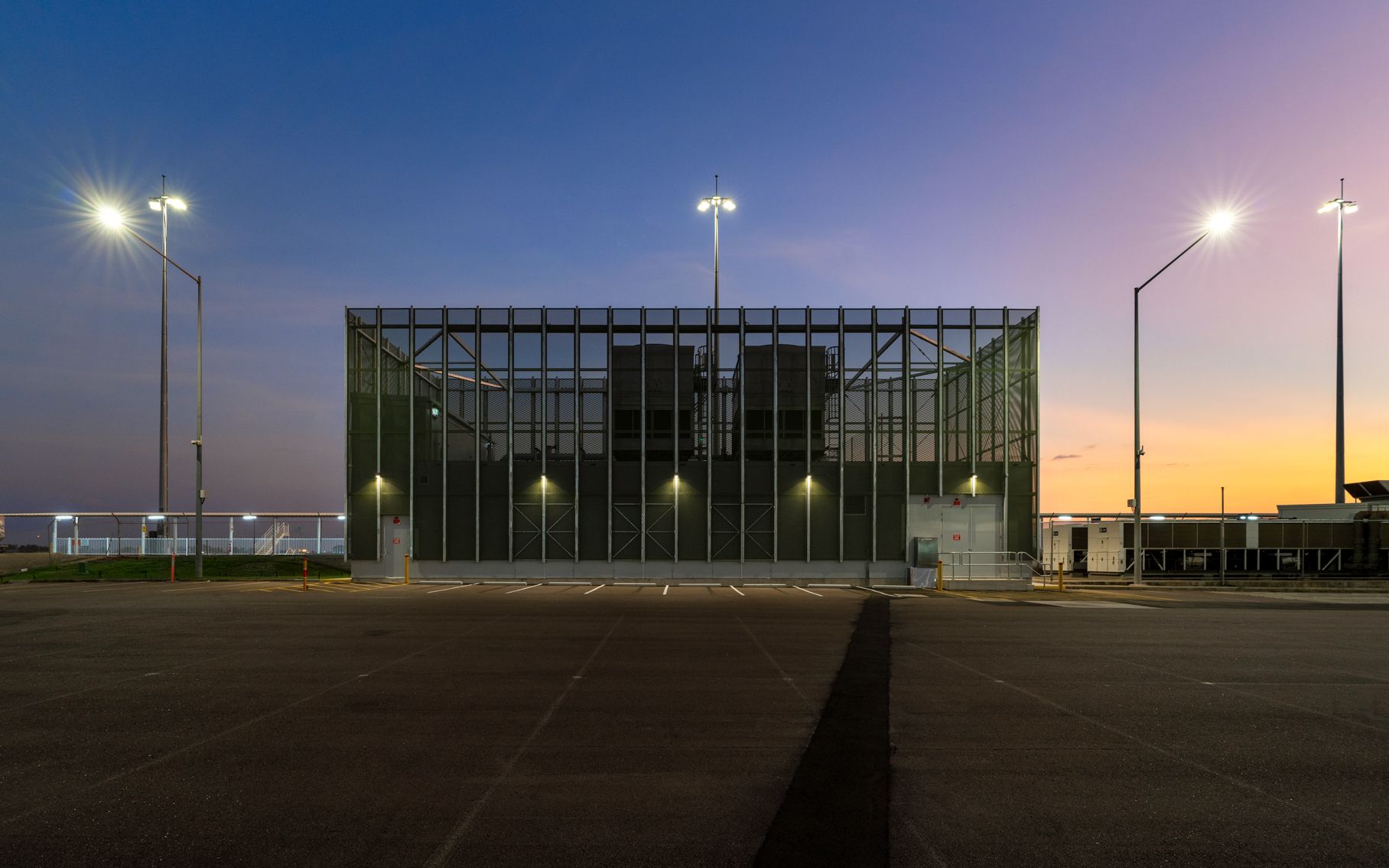 Building with caged exterior at dusk, with parking lot in the foreground and streetlights illuminating the scene.