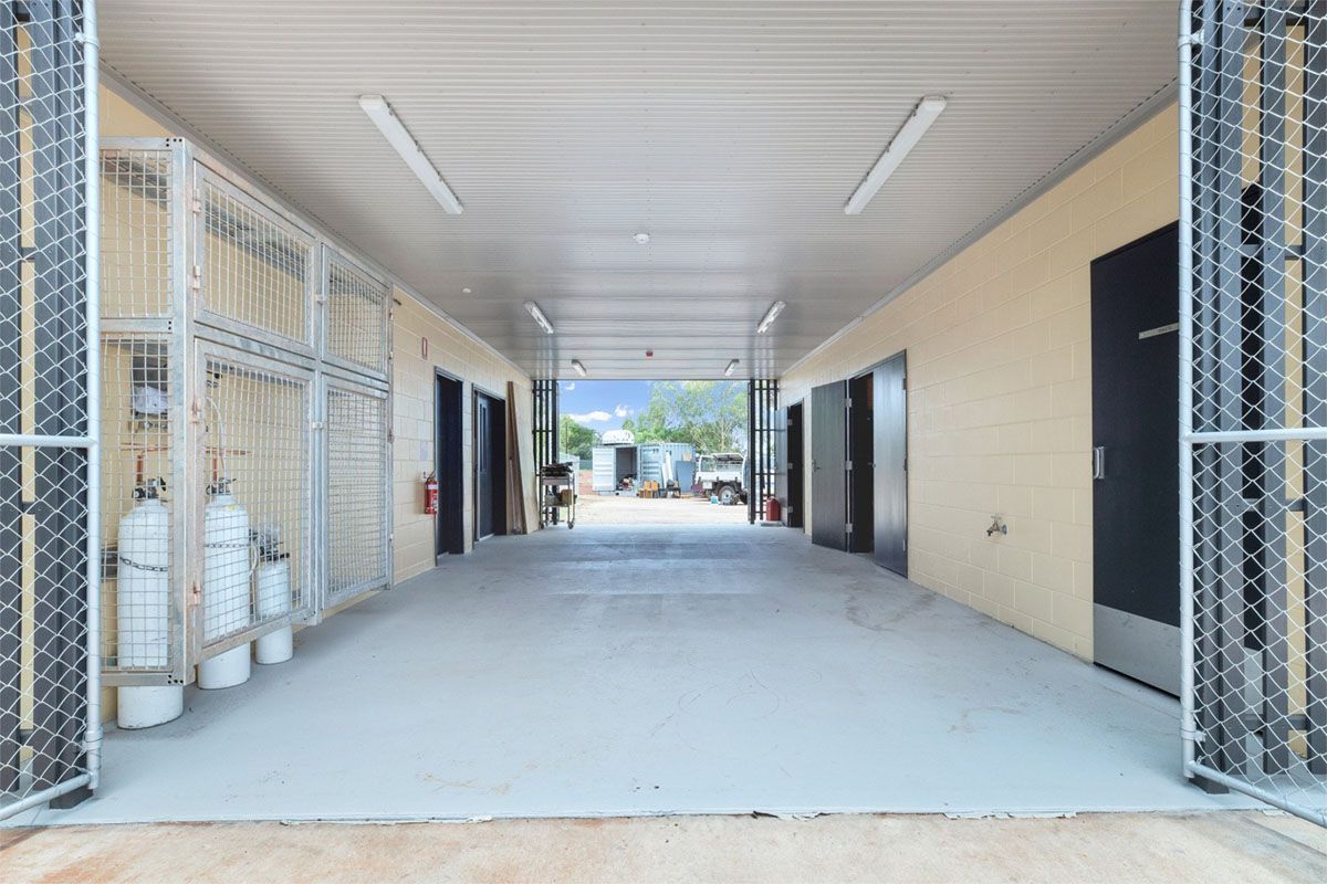 A long, covered hallway with doors, metal fencing, and bright lights.