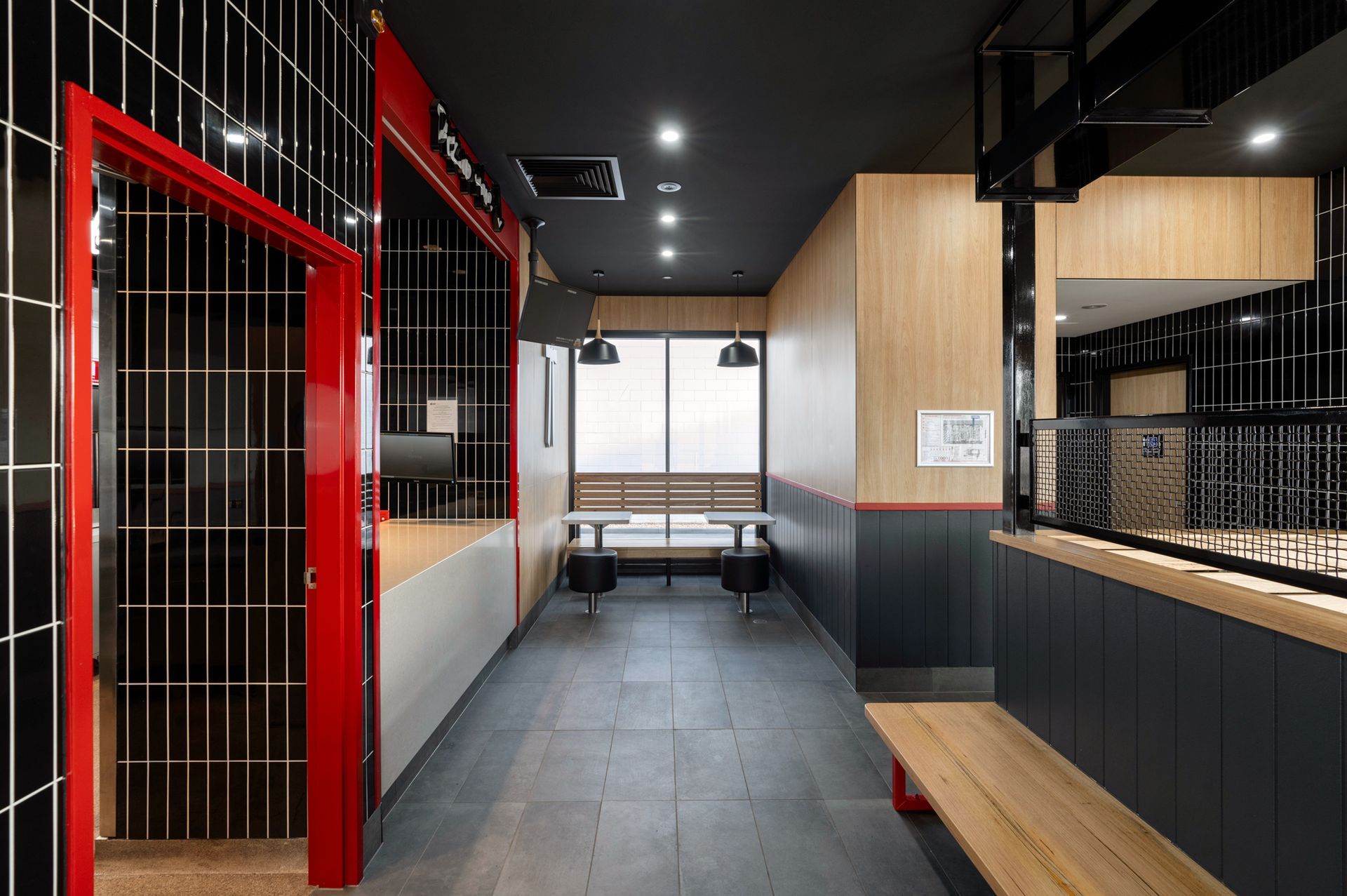Interior view of a restaurant with a red and black color scheme, bench seating, and a long hallway.