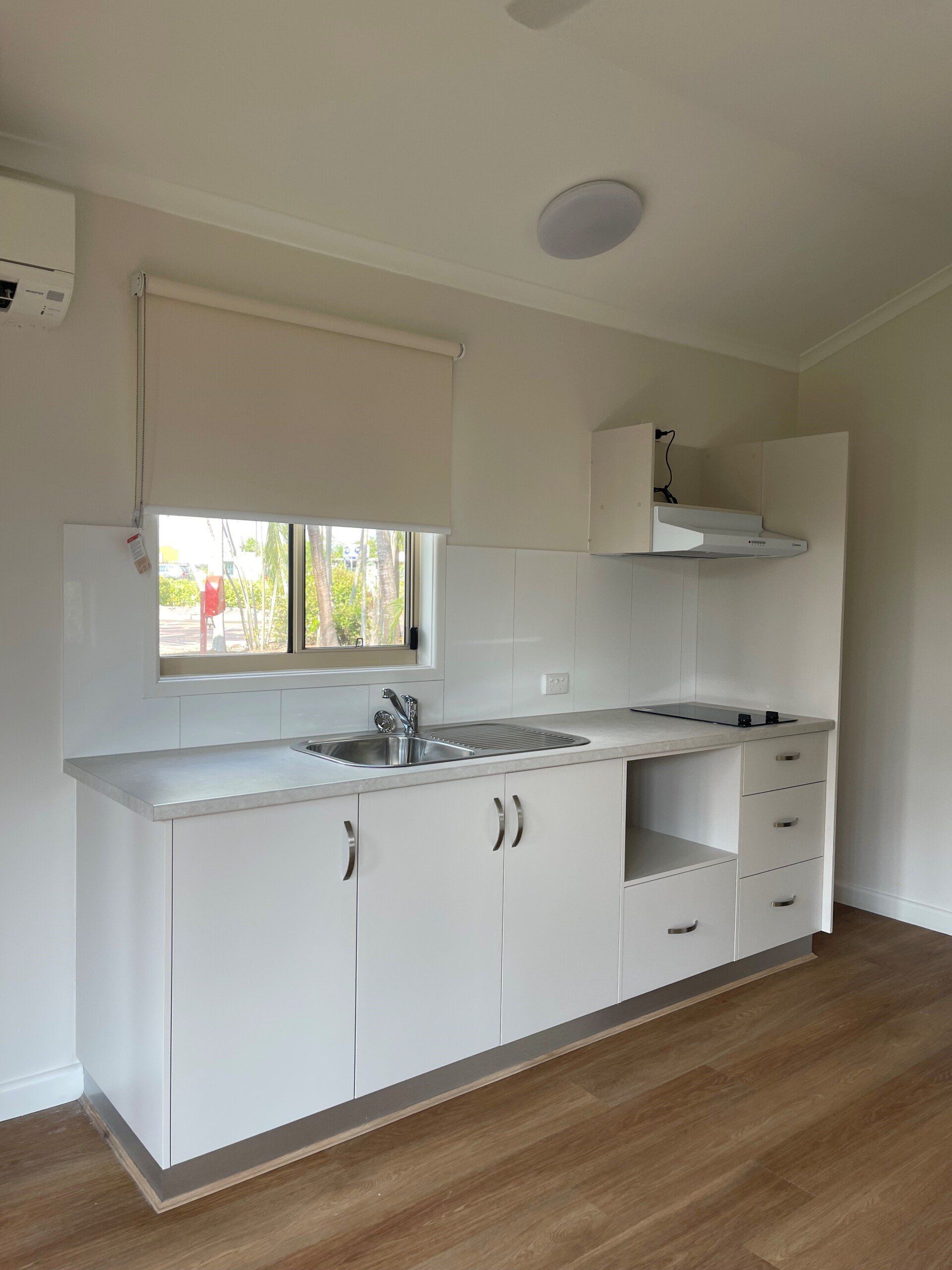 Small white kitchen with cabinets, sink, stove, window, and range hood.