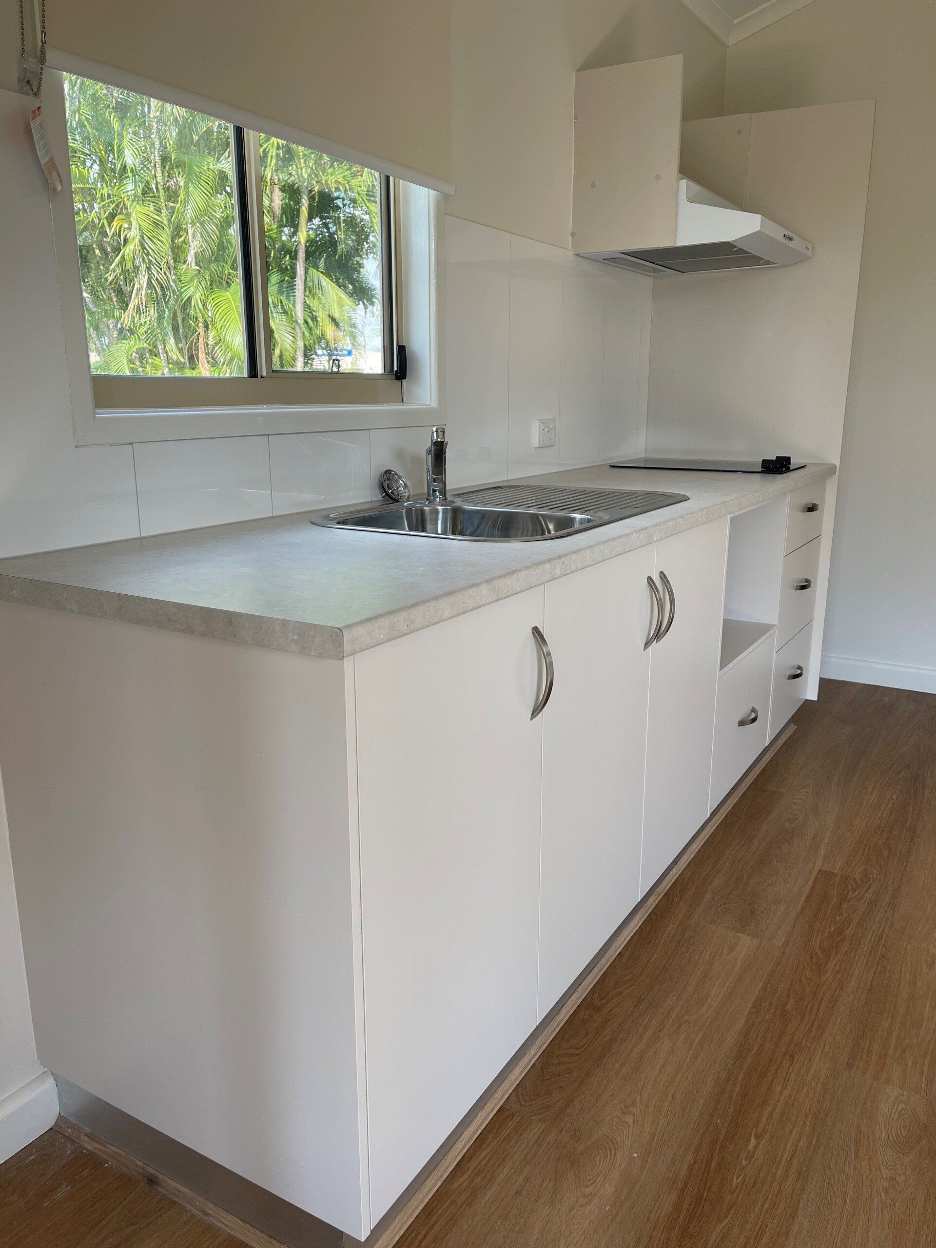 White kitchen with sink, stovetop, and cabinets, next to a window.