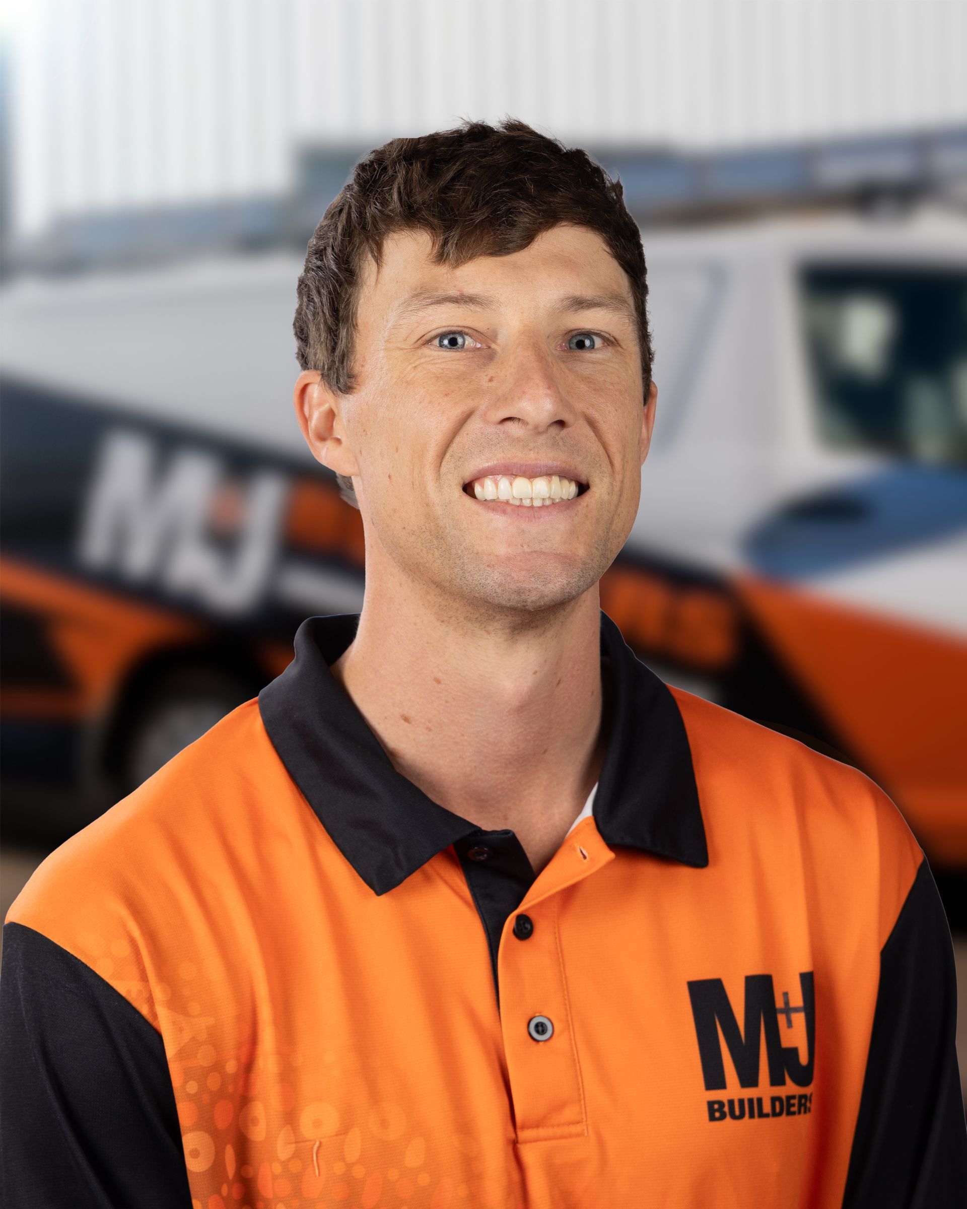Man smiling in orange and black work shirt, background of truck.