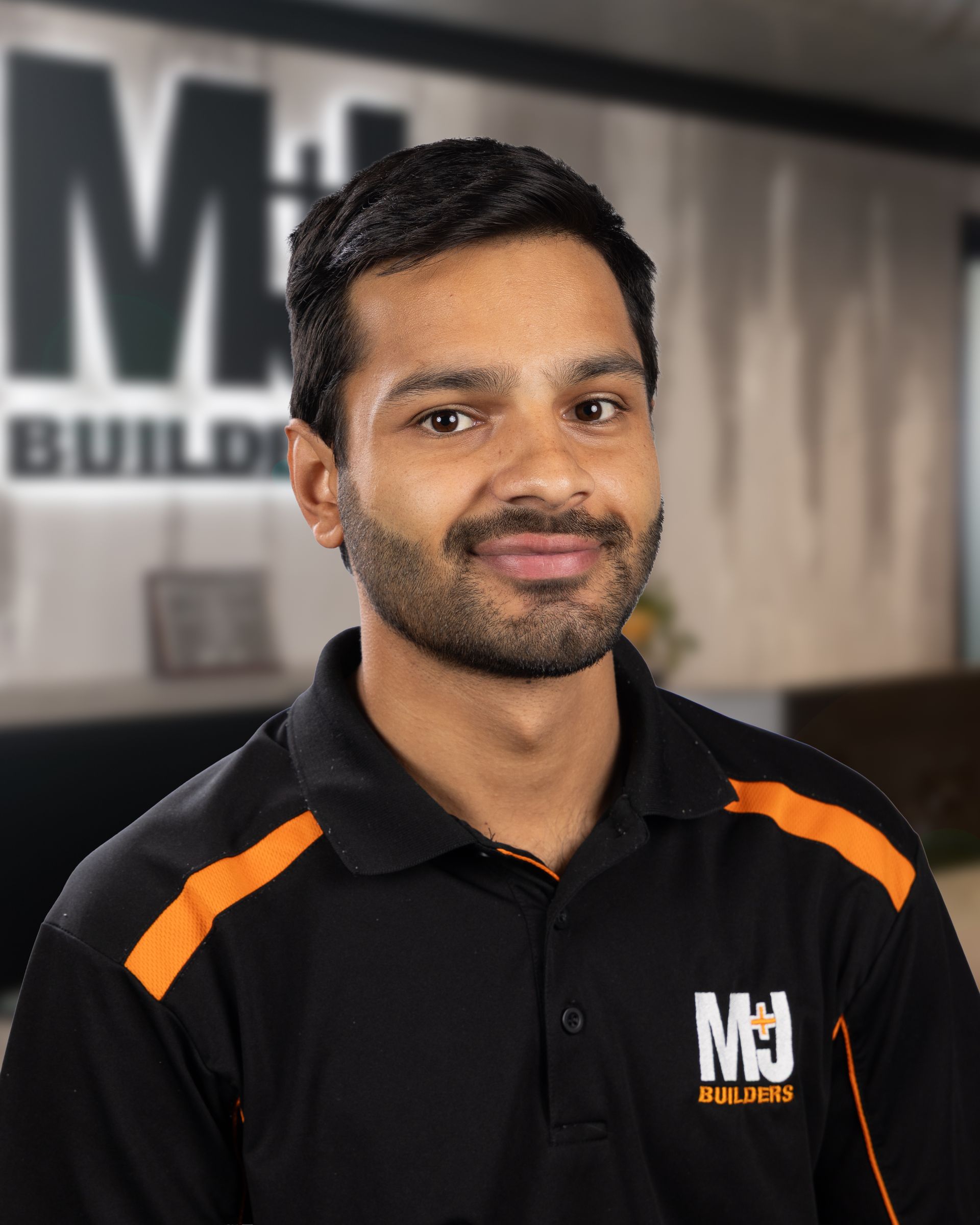 Man with dark hair, wearing black polo shirt with orange accents, smiling.