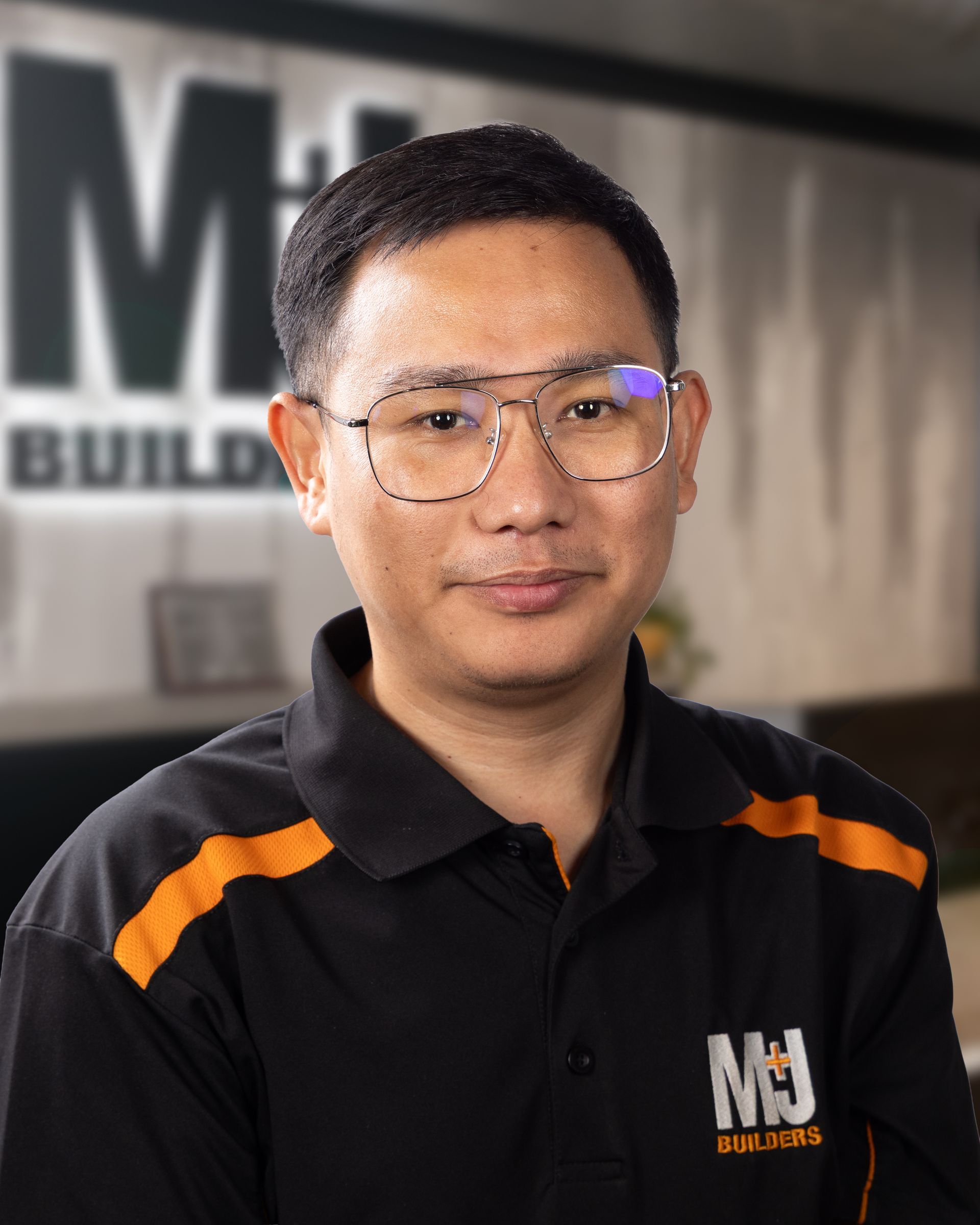 Man with glasses in a black polo shirt with orange accents, smiling at the camera.