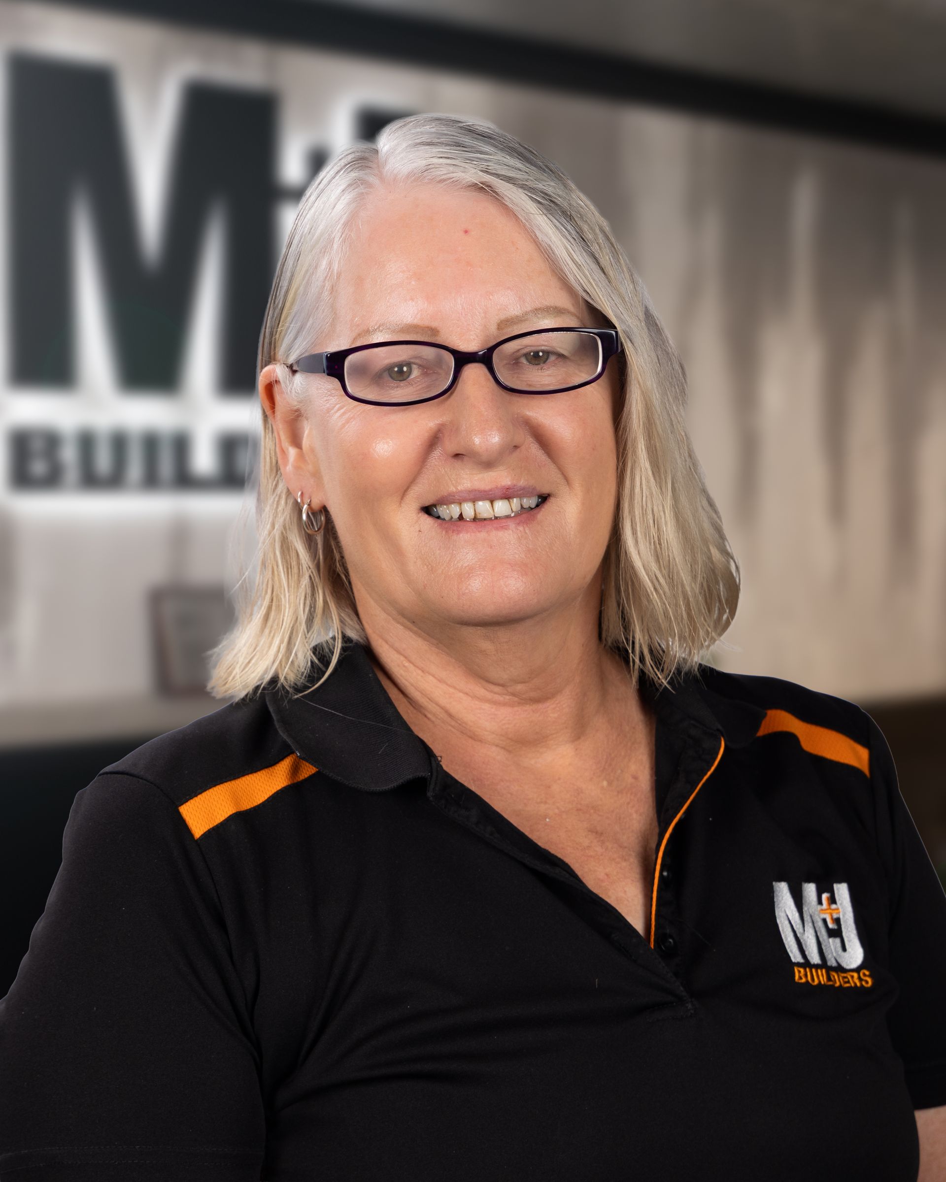 Woman with blonde hair and glasses wearing a black polo shirt smiles at the camera.