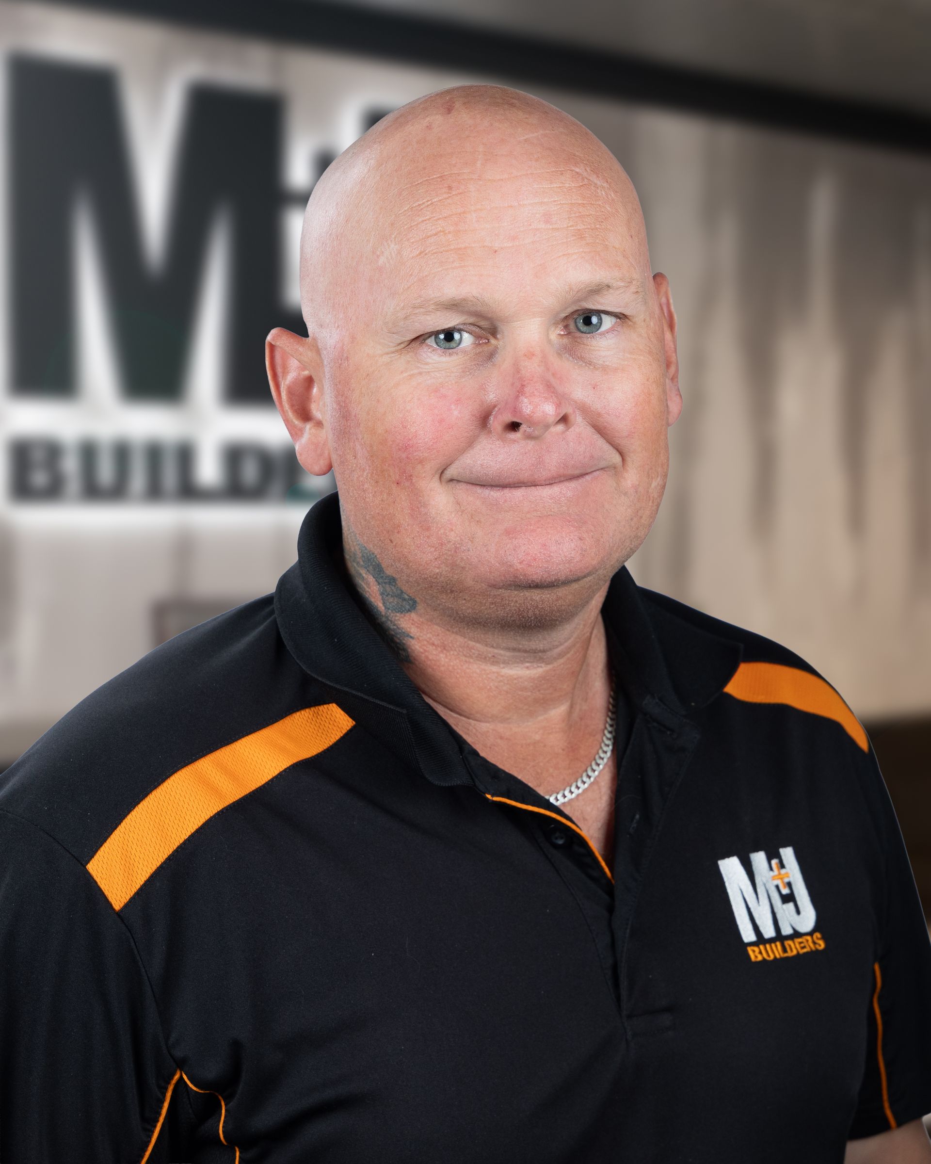 Bald man wearing a black polo shirt with orange accents, the shirt has