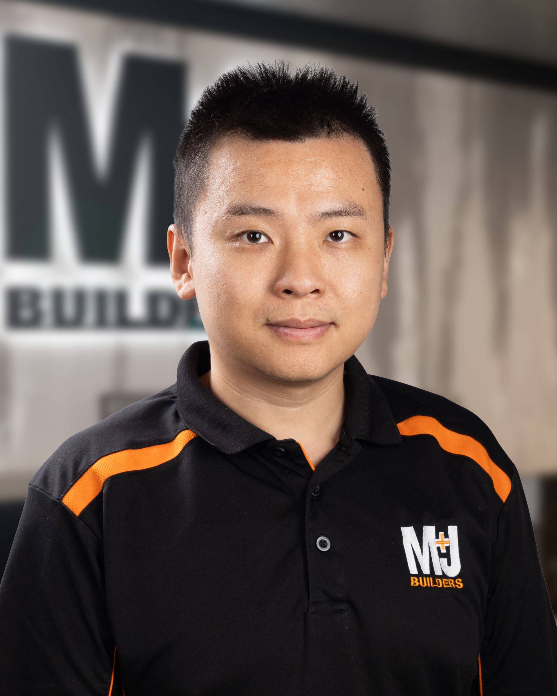 Asian man wearing a black MJ Builders polo shirt, looking at the camera.