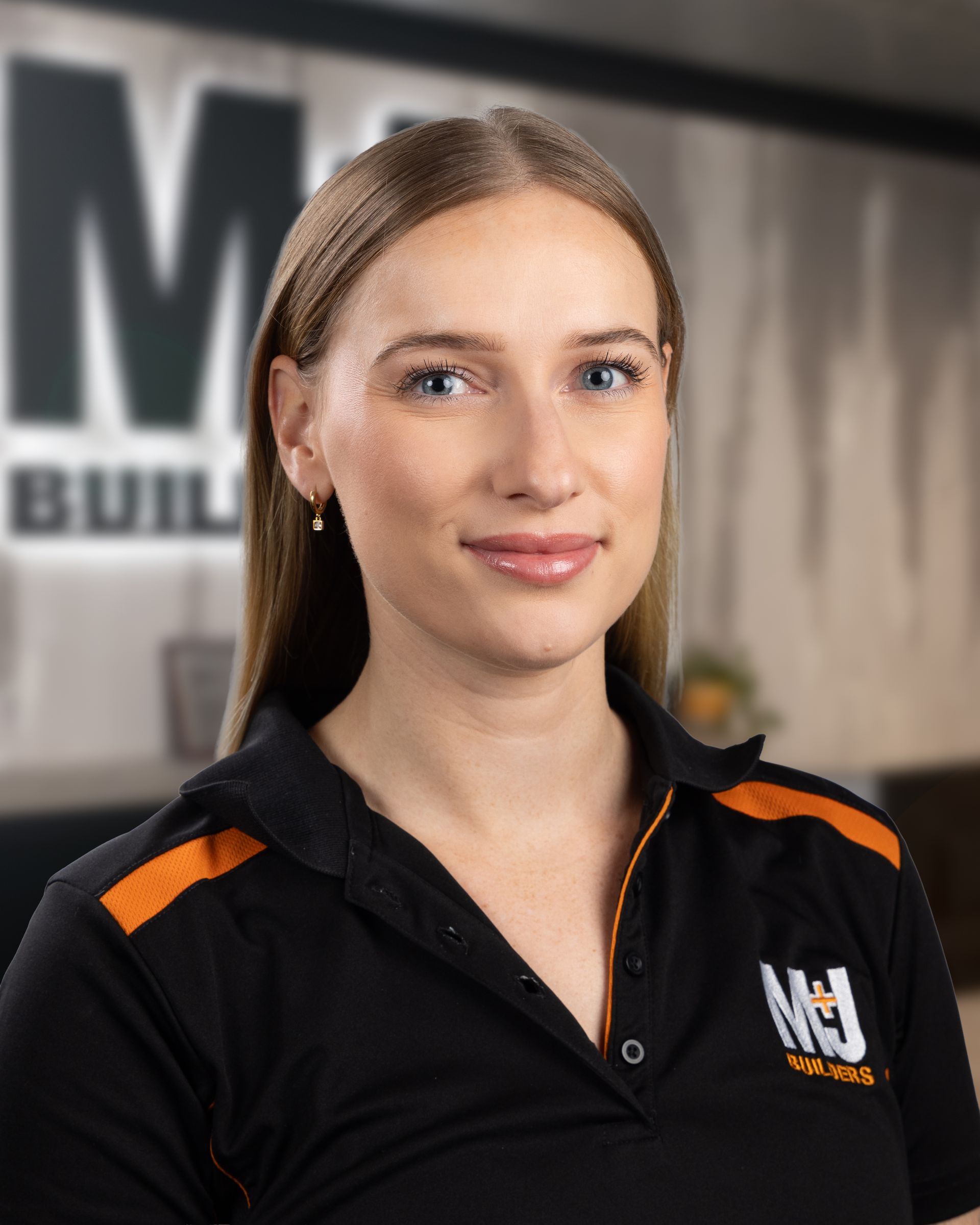 Blonde woman in black polo shirt with orange accents, logo on chest, looking at the camera.