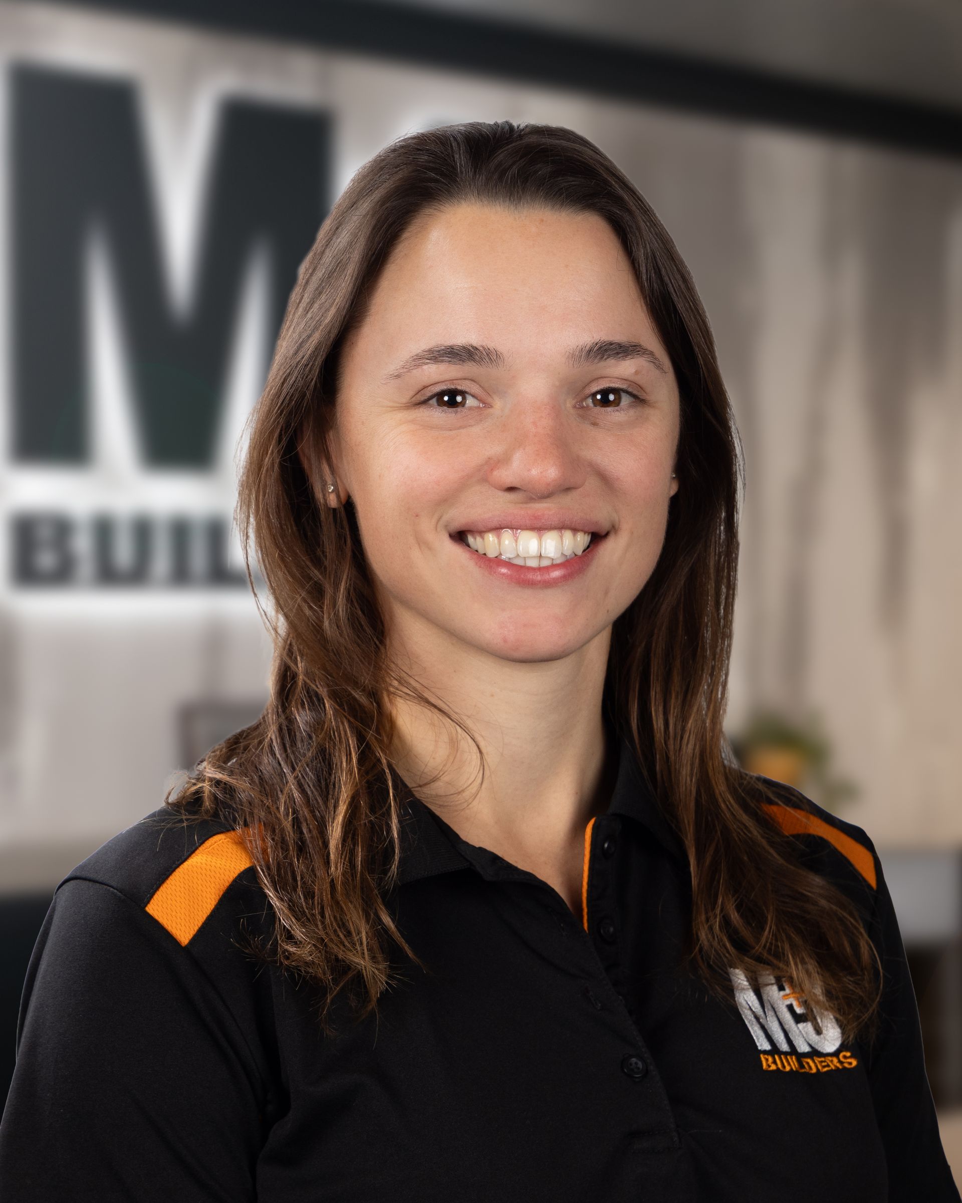 Woman with light brown hair, smiling, wearing a black polo shirt with orange accents and a logo.