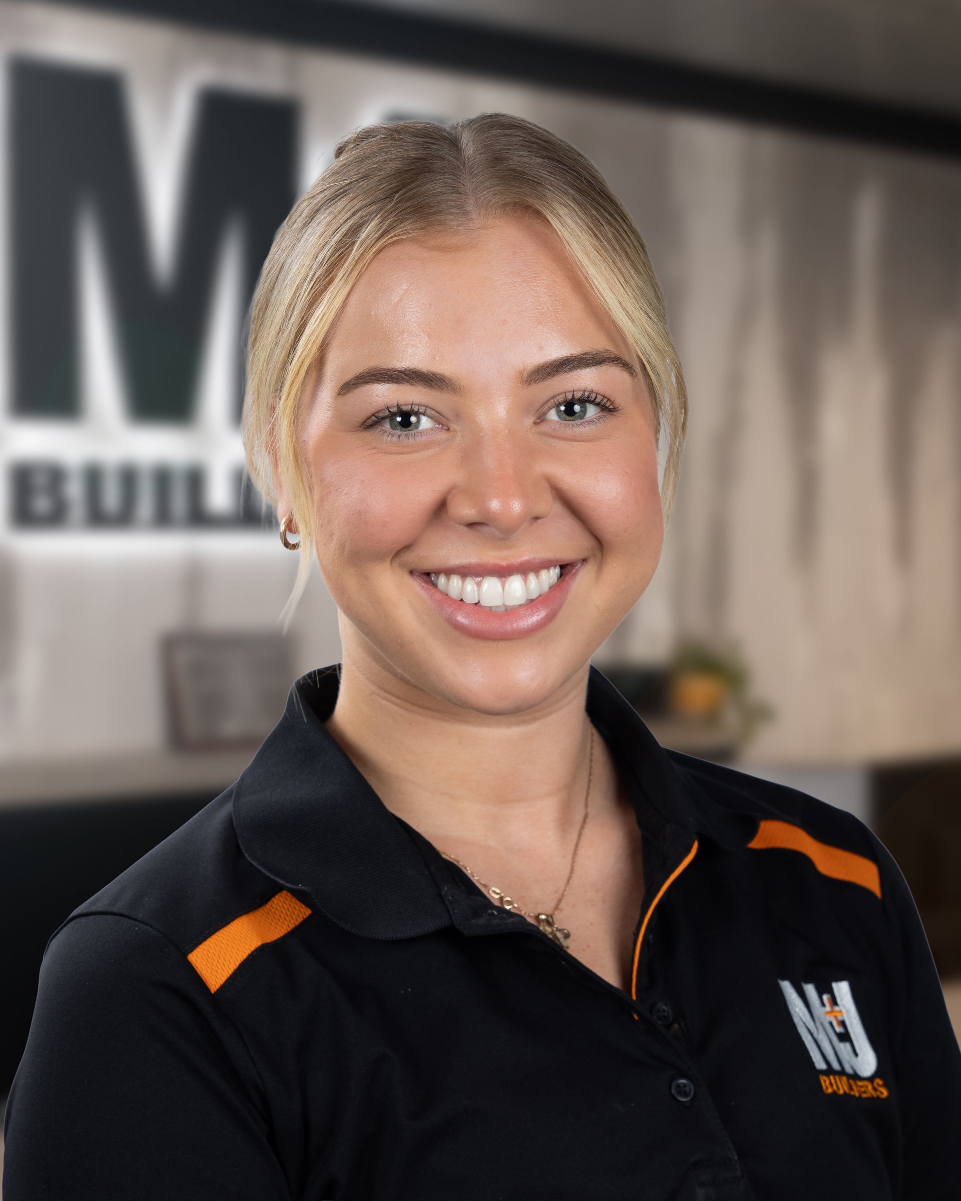 Blonde woman smiling in black polo shirt with orange accents and logo.