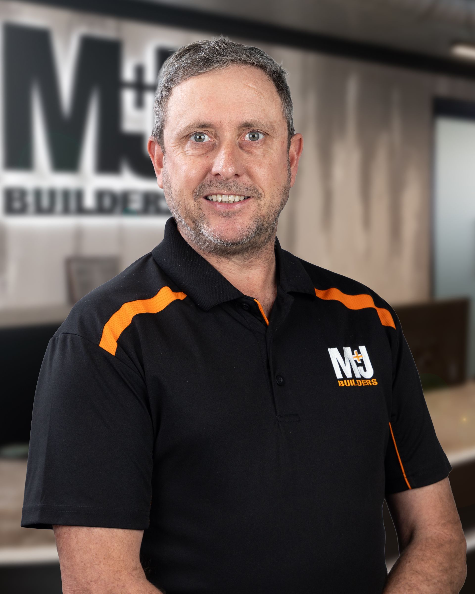 Man in black polo shirt with orange accents and MJ Builders logo.
