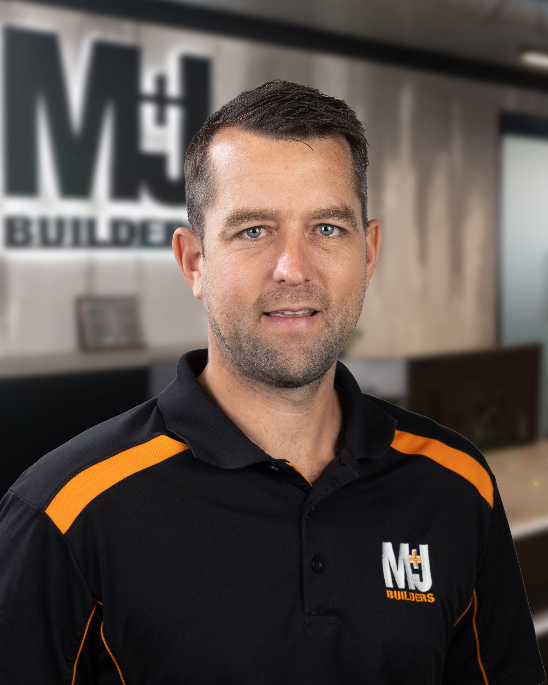 Man with short brown hair wearing a black and orange polo shirt smiling at the camera.