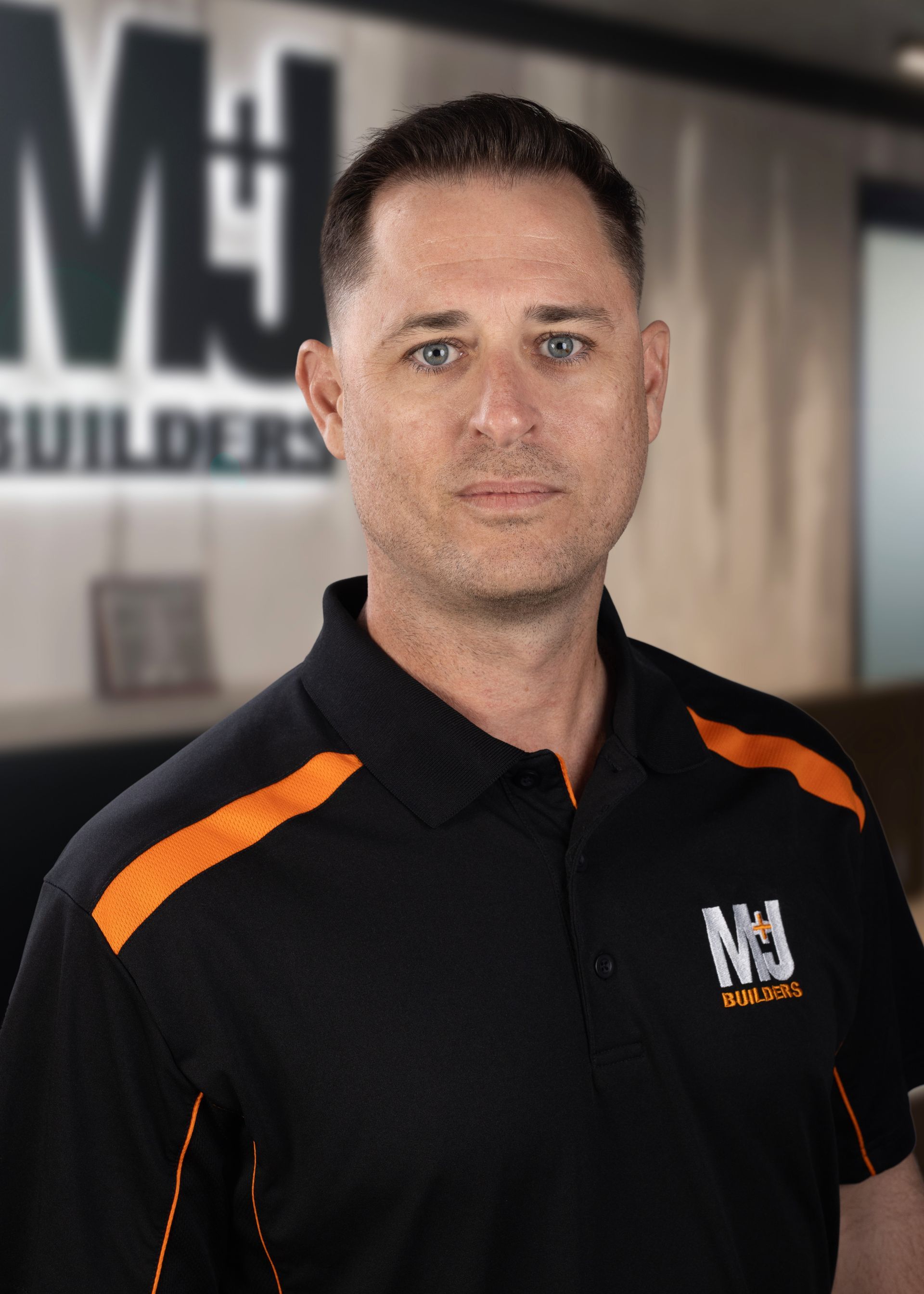 Man in black polo shirt with orange accents, looking at the viewer. The shirt displays the logo