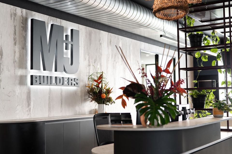 M+J builders sign inside the headoffice on a rendered concrete wall with plants and greenery surrounding
