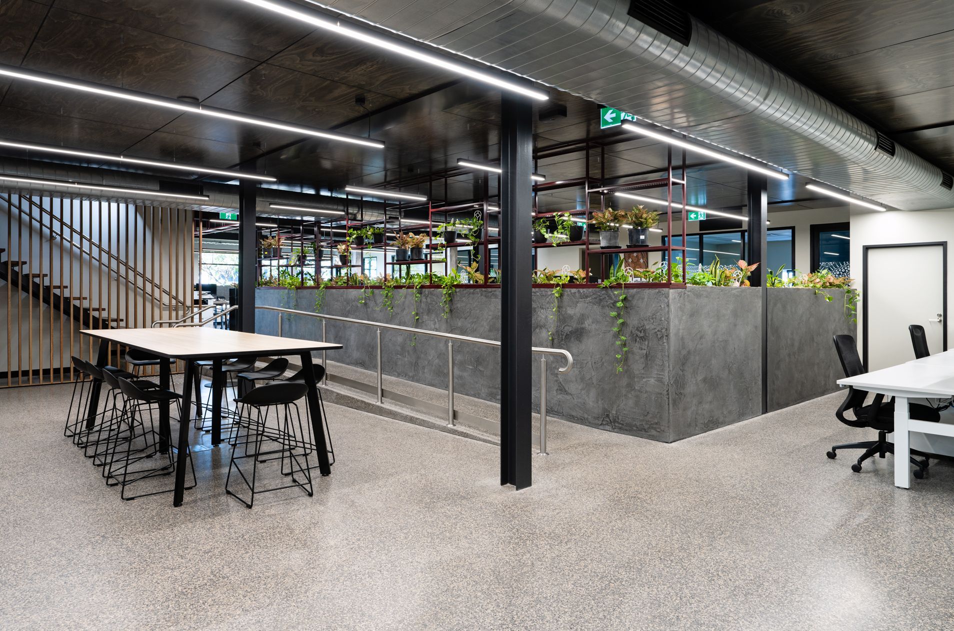 Modern office space with tables, chairs, and a long planter wall filled with greenery.