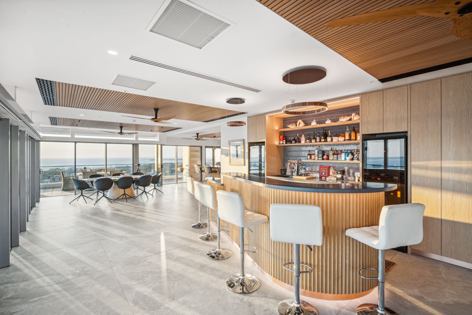 Luxurious bar with wooden accents and white bar stools, overlooking an ocean view.
