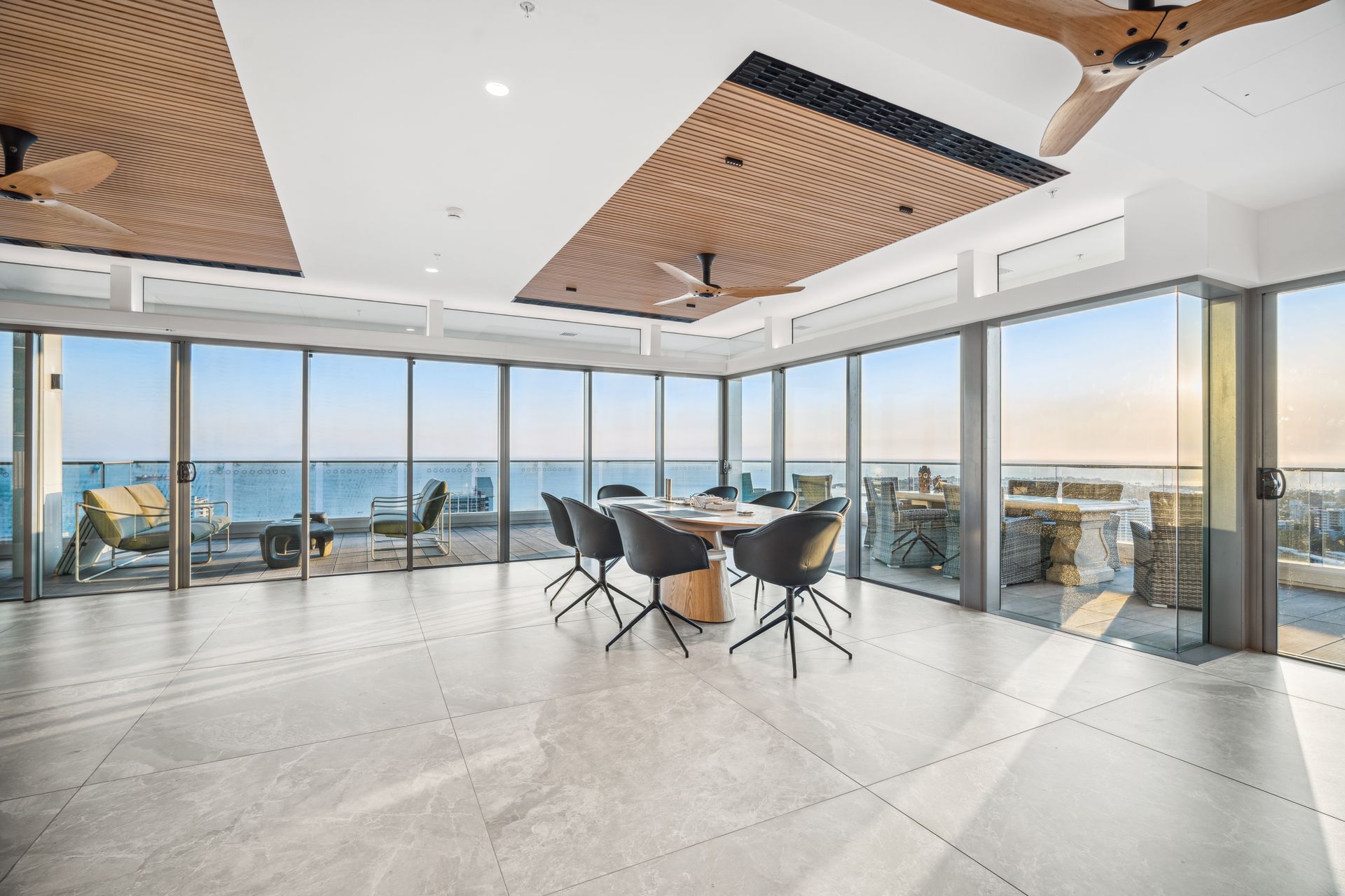 Modern office with panoramic ocean view, glass walls, and a large conference table.