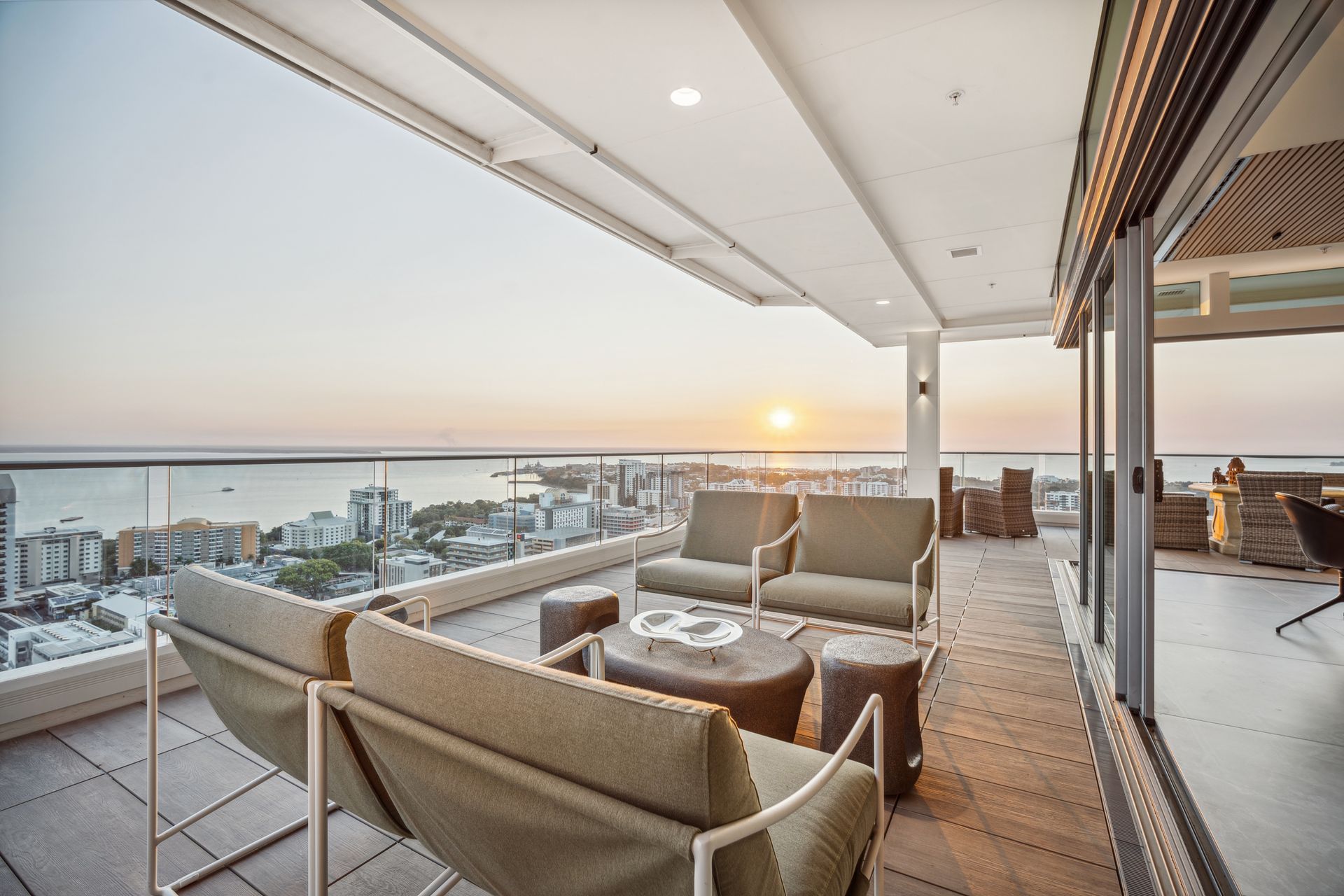 Rooftop patio with seating overlooking a city and ocean at sunset.