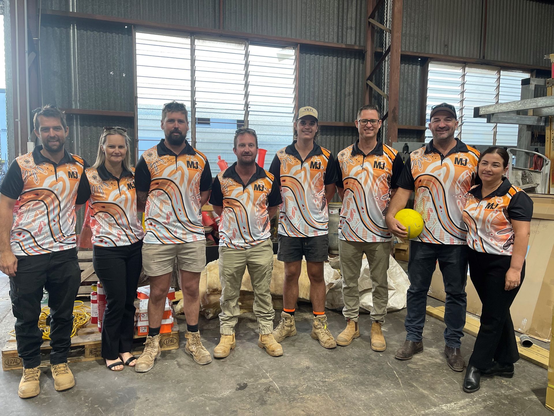 Group of nine people wearing matching shirts poses inside a warehouse.