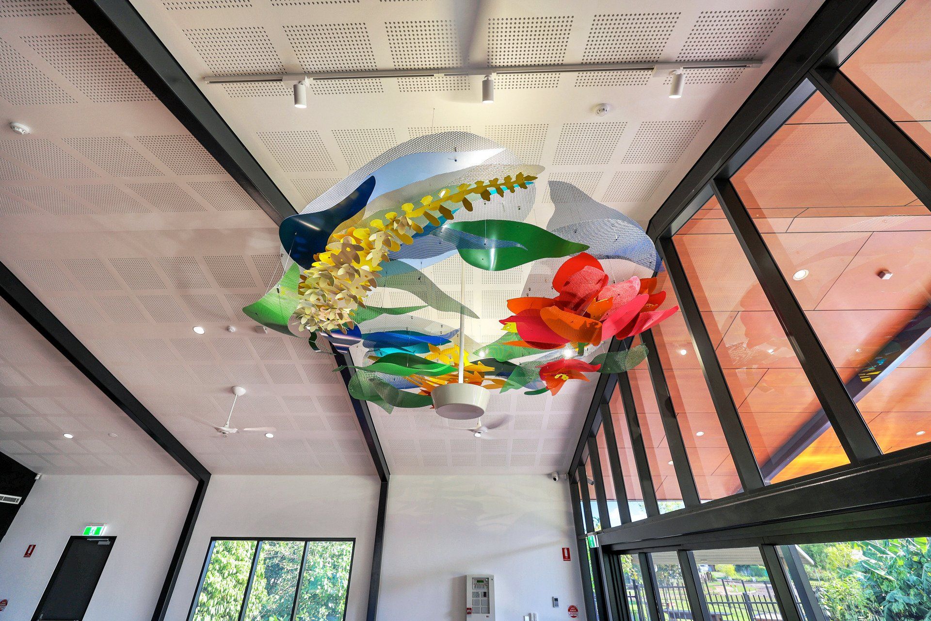 A colorful, suspended floral sculpture hangs in a bright gallery space with large windows.